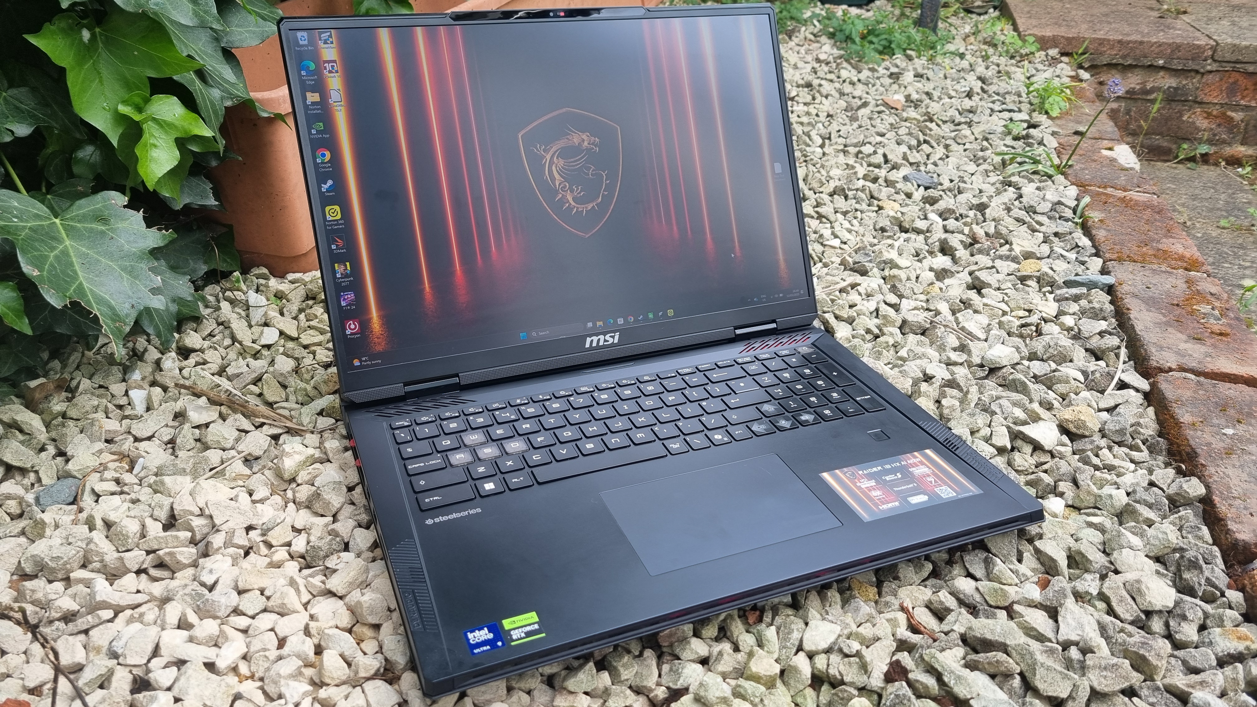 The MSI Raider 18 HX AI A2XW open on white gravel in a garden that's far too small for the occupants of the house