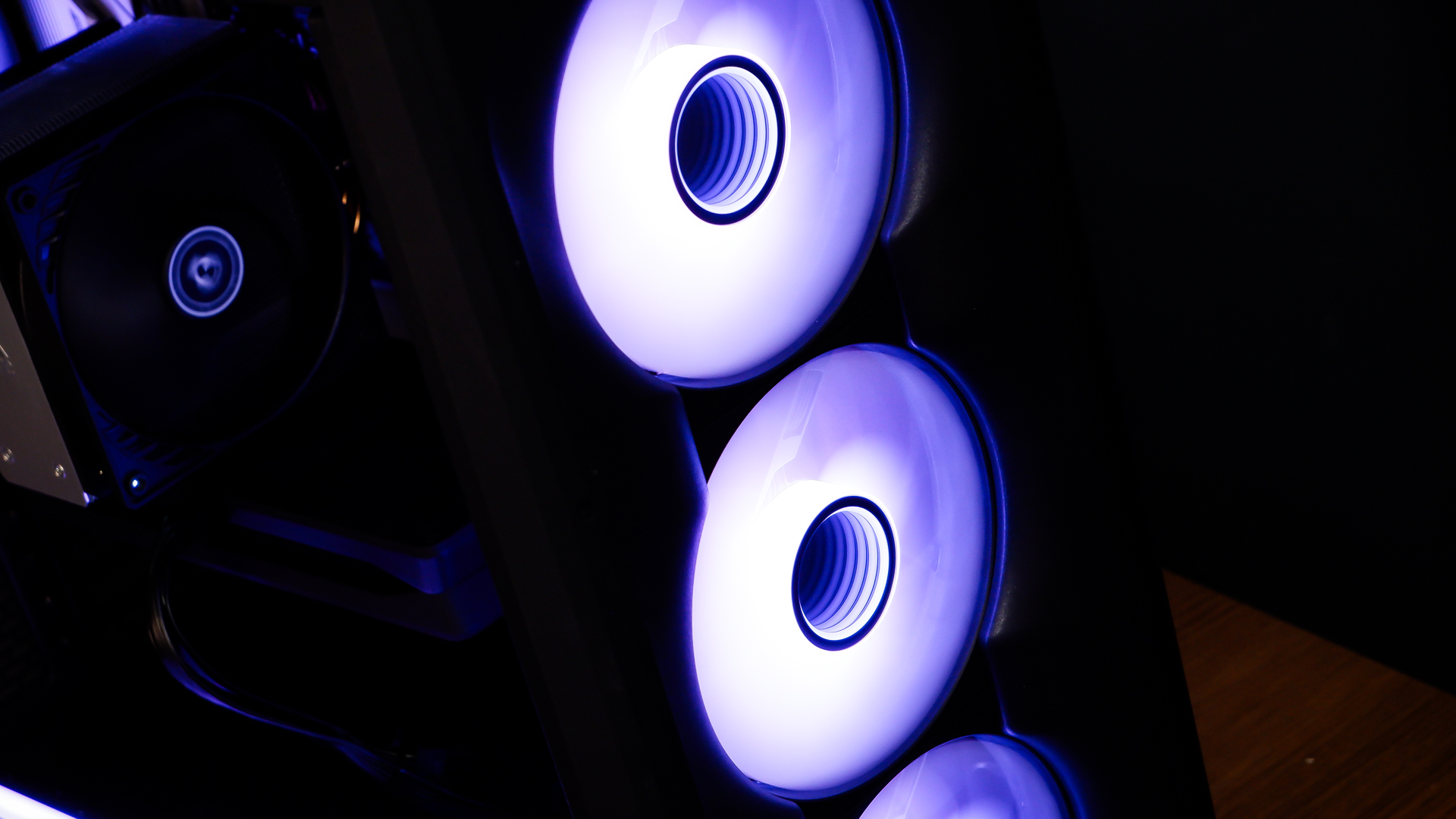 A gaming PC sat on a desk with purple RGB lighting on the fans and light bar enabled.