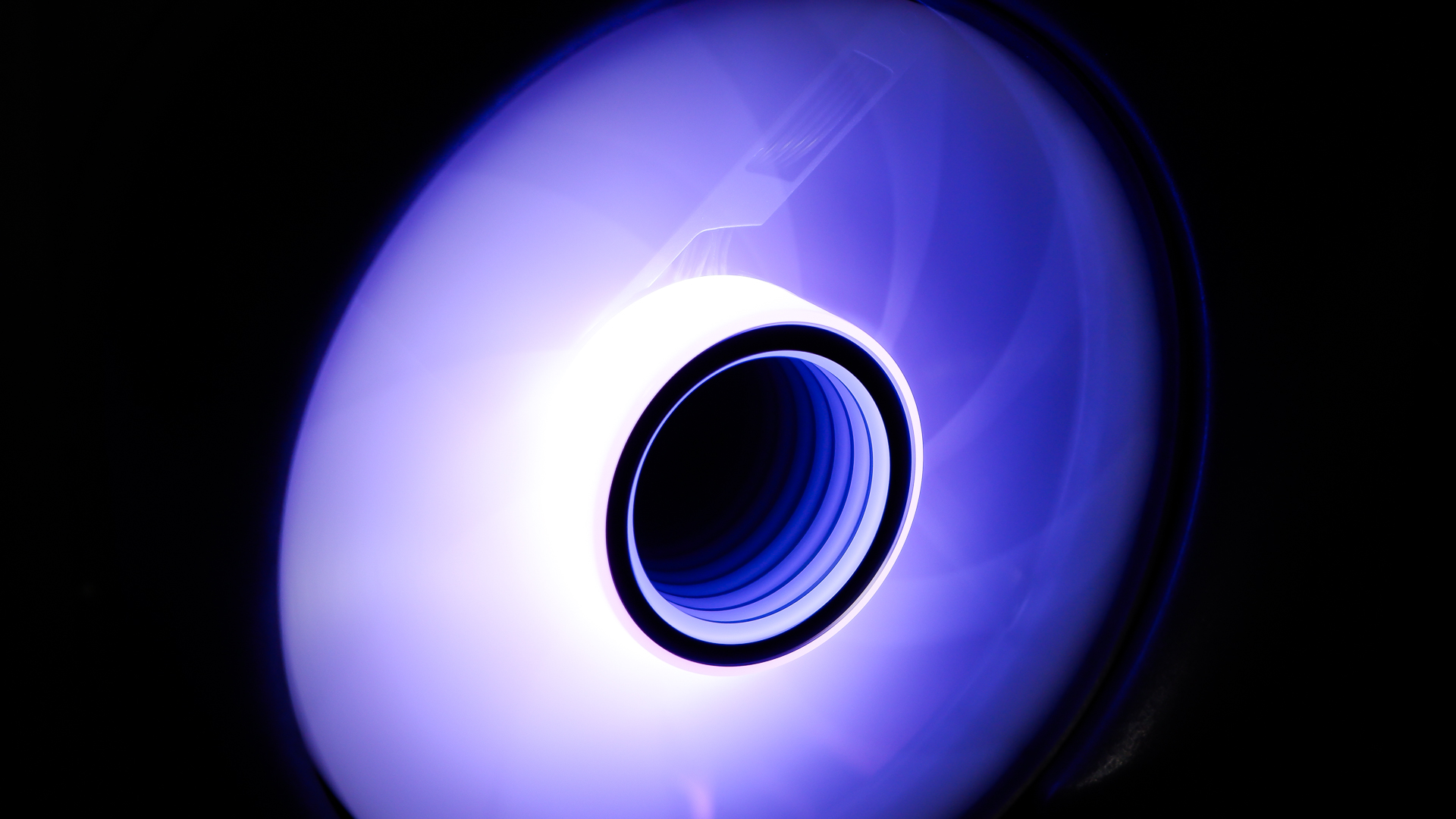 A gaming PC sat on a desk with purple RGB lighting on the fans and light bar enabled.