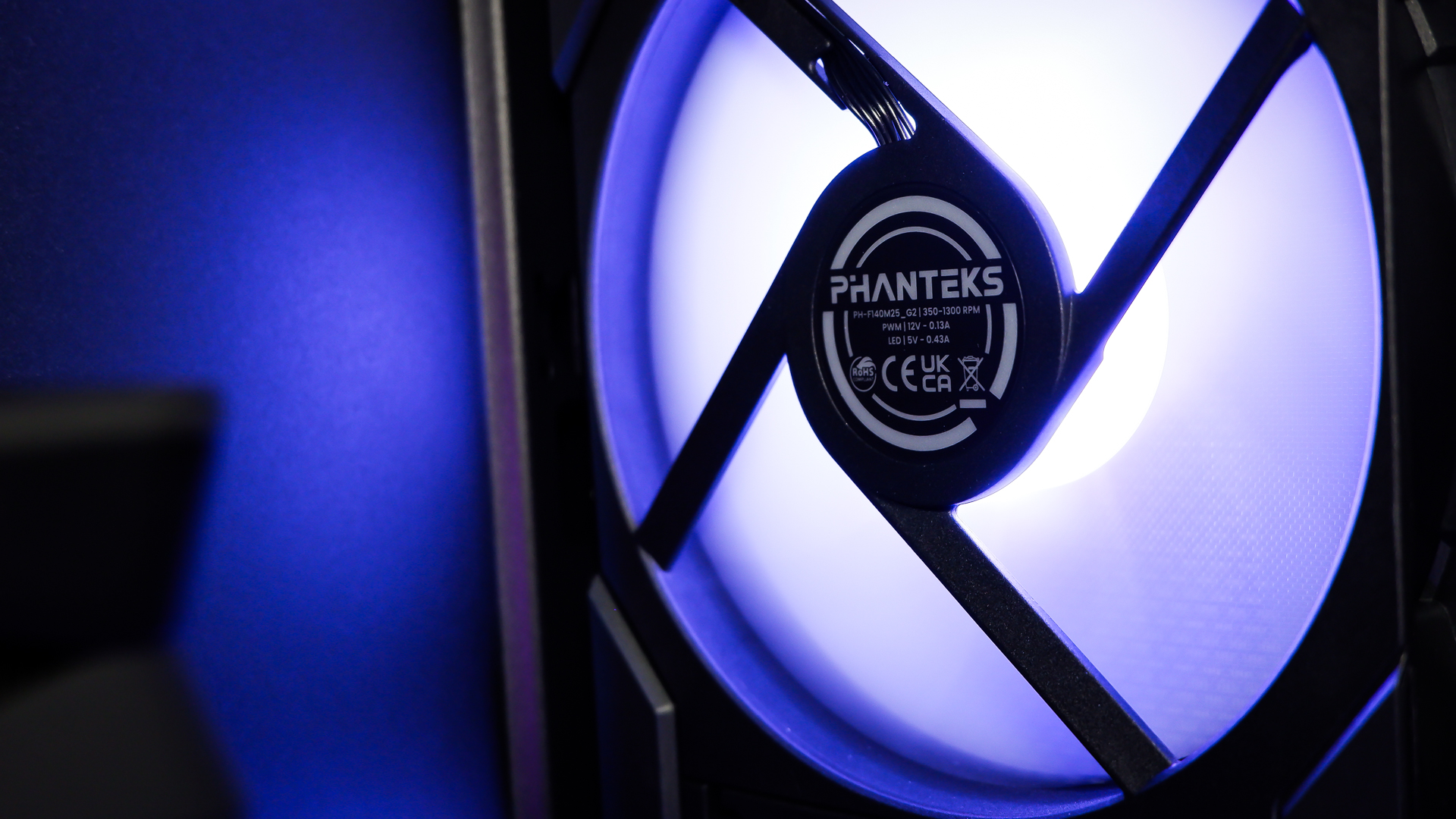 A gaming PC sat on a desk with purple RGB lighting on the fans and light bar enabled.