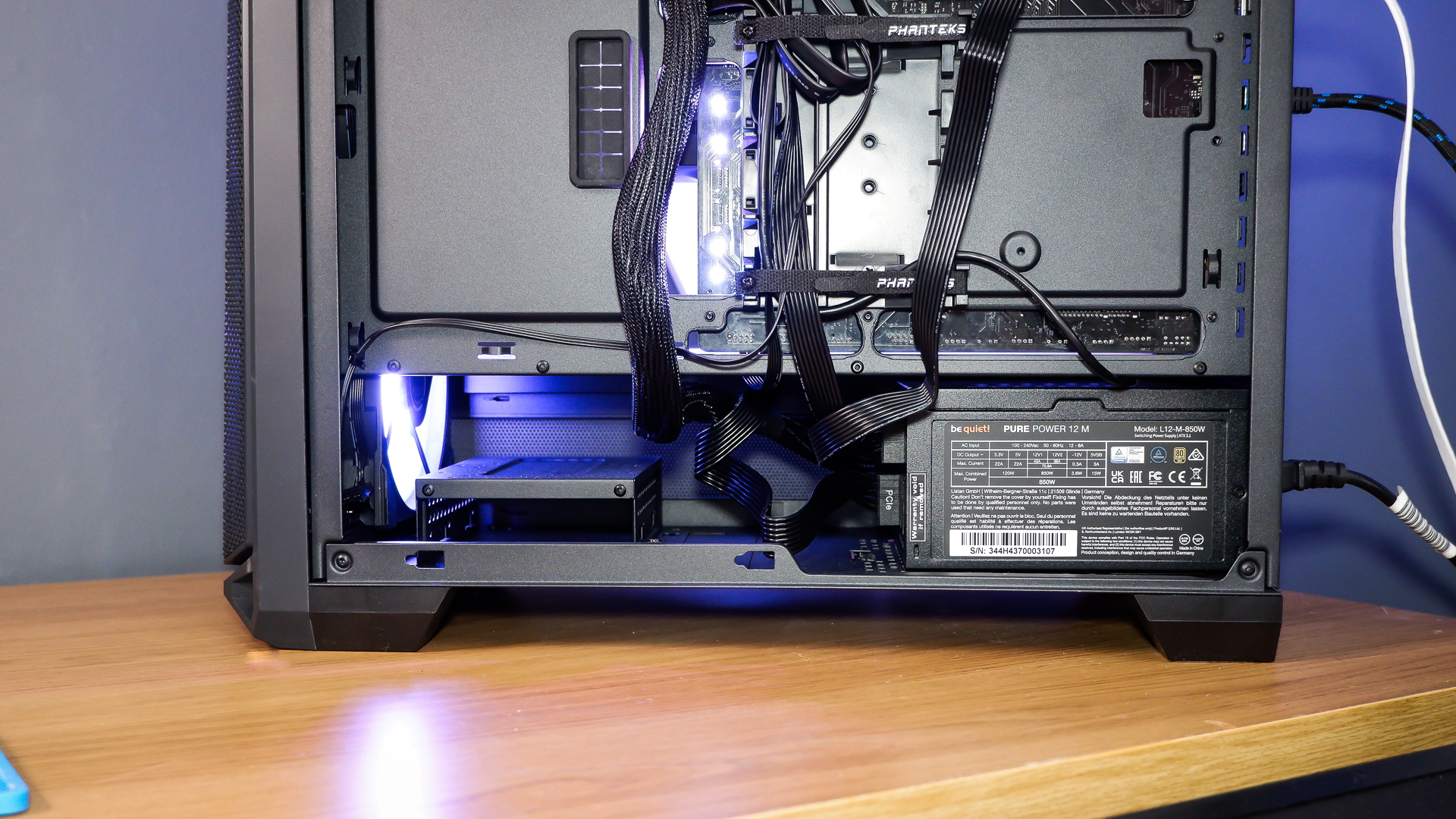 A gaming PC sat on a desk with purple RGB lighting on the fans and light bar enabled.