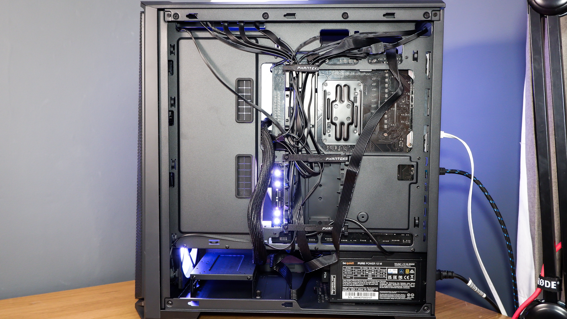 A gaming PC sat on a desk with purple RGB lighting on the fans and light bar enabled.