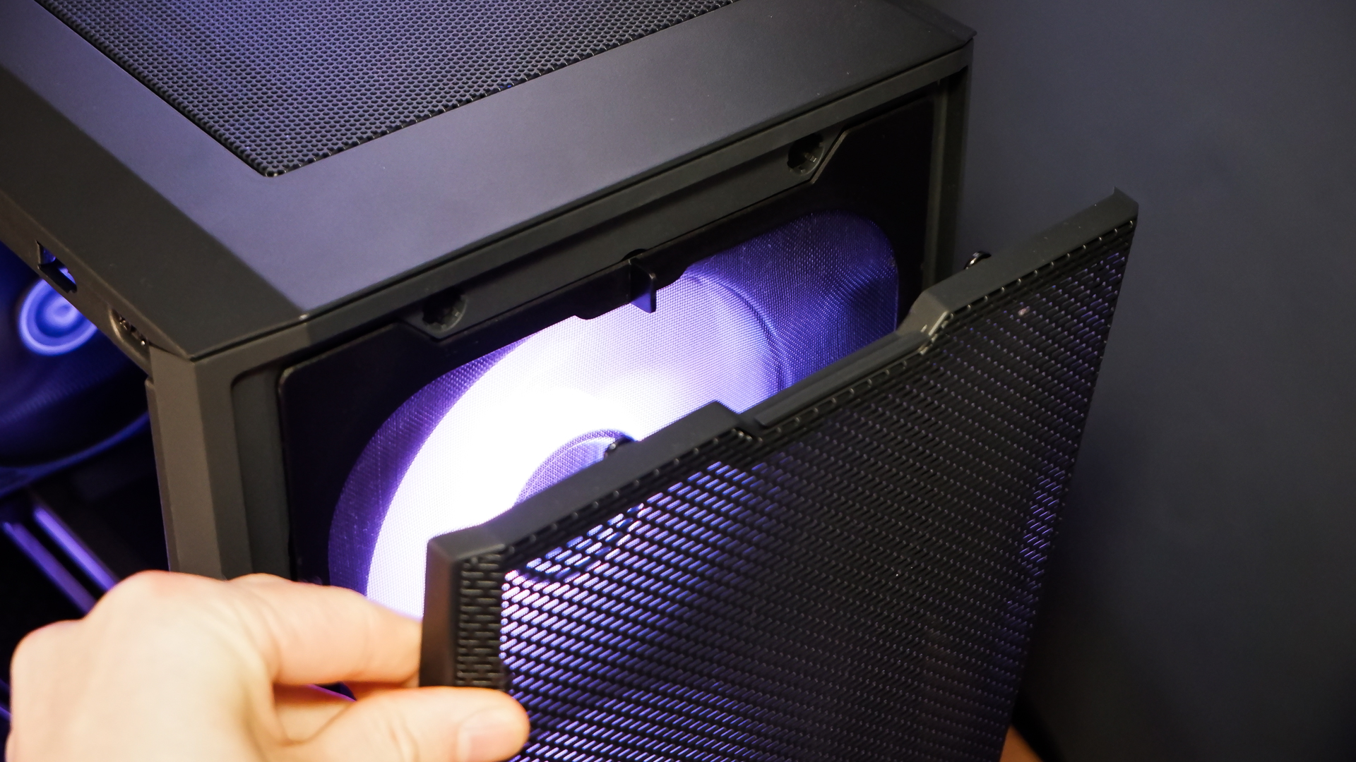 A gaming PC sat on a desk with purple RGB lighting on the fans and light bar enabled.