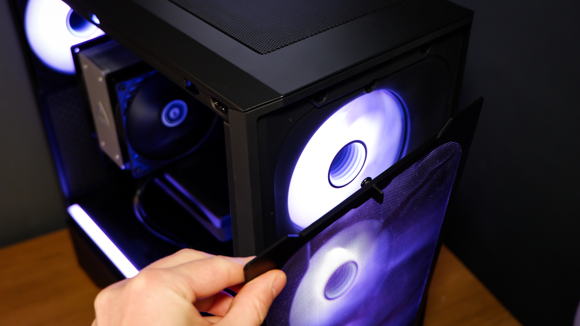 A gaming PC sat on a desk with purple RGB lighting on the fans and light bar enabled.