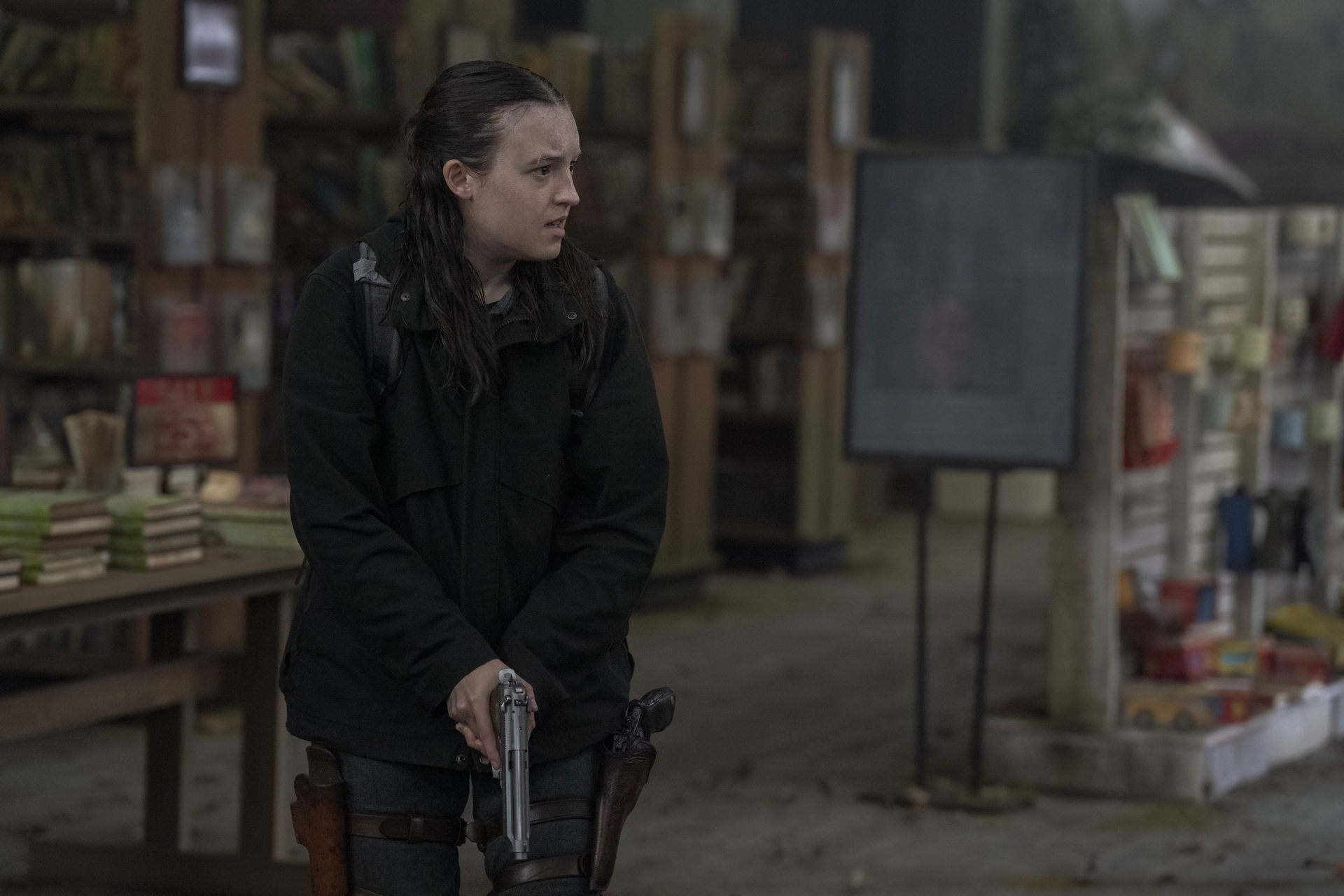 Ellie from The Last of Us show stands in a run-down library, holding a gun Ellie from The Last of Us show stands in a run-down library, holding a gun