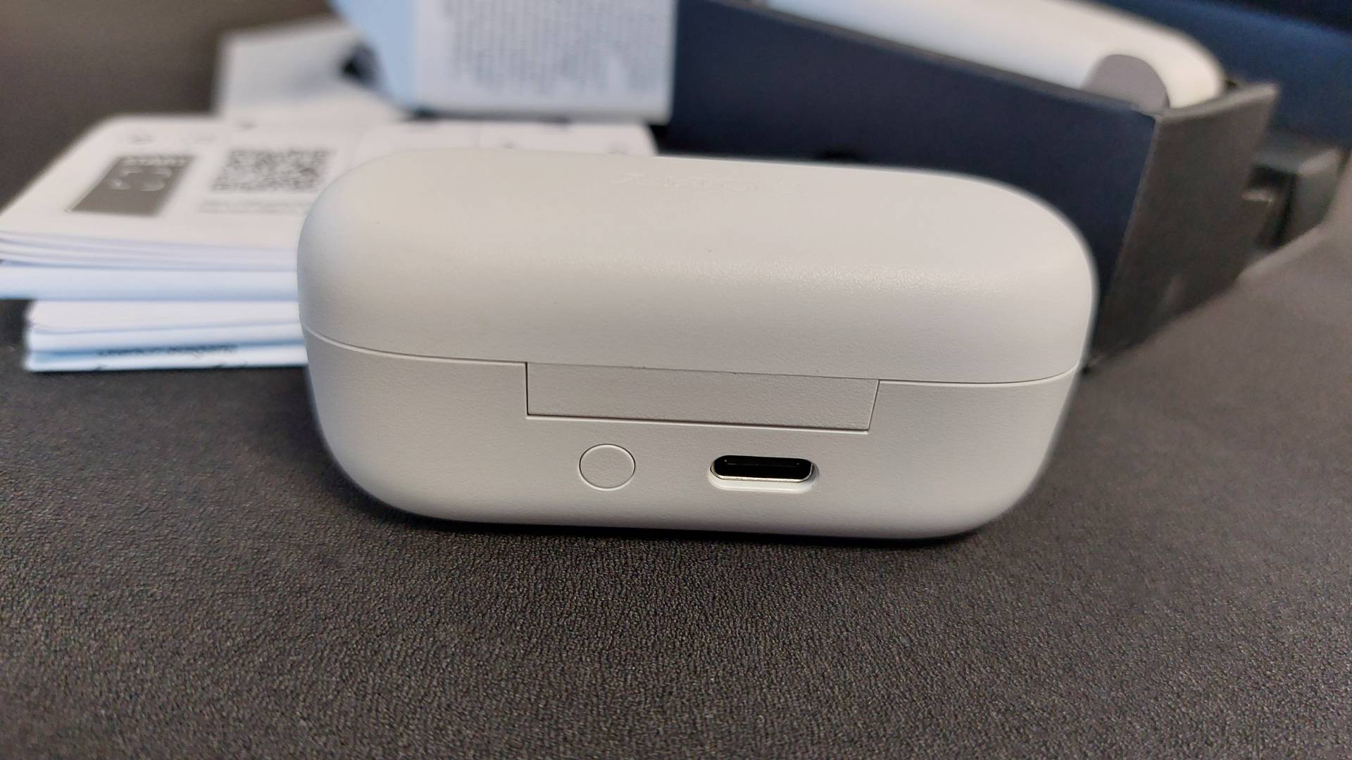 The Sony WF-C510 earbuds on a black desk mat. They are seen here inside their sleek charging case. This image focusses on the back, showing the pairing button and USB-C charging port.