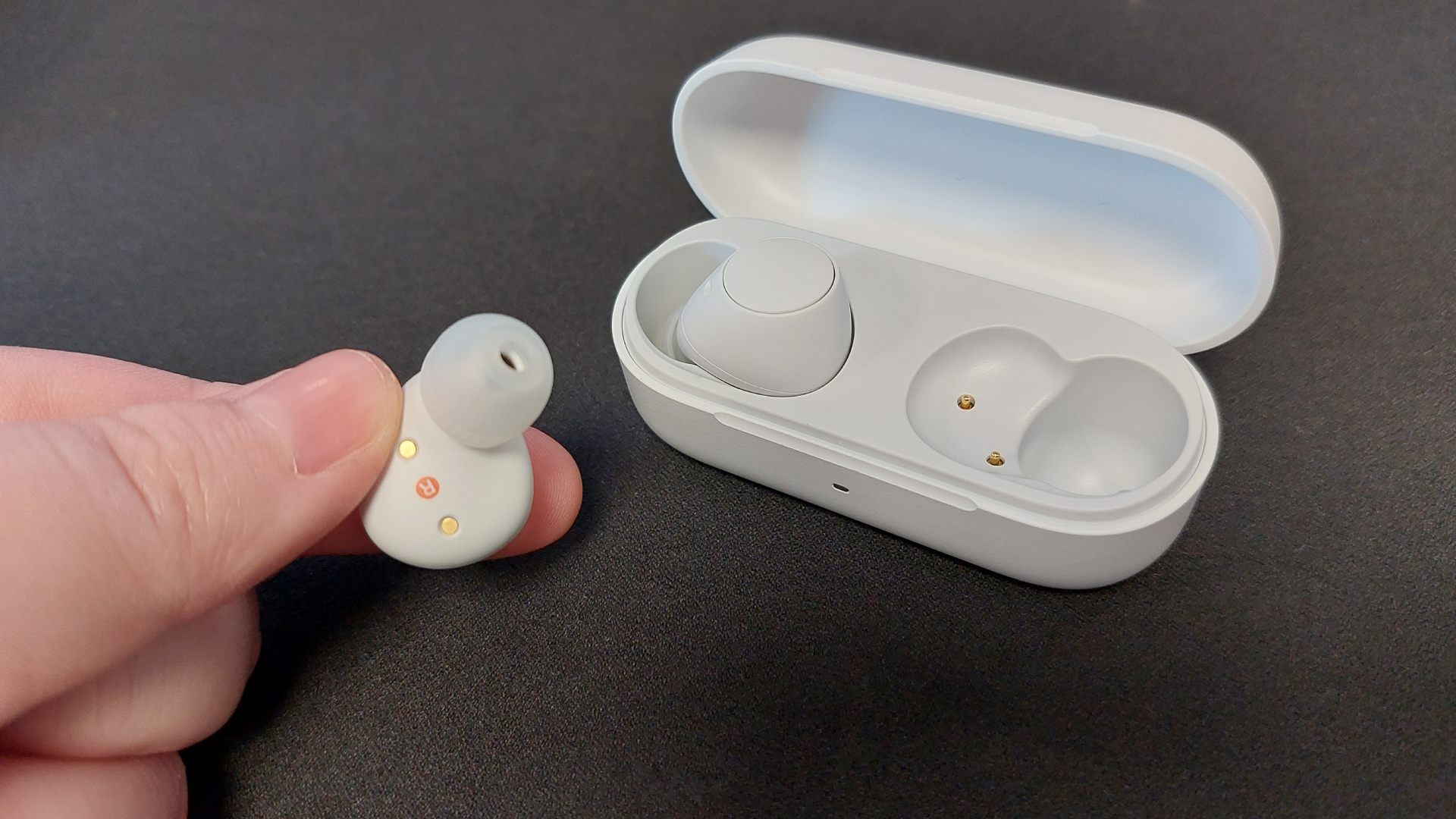 The Sony WF-C510 earbuds on a black desk mat. They are seen here inside their sleek charging case.