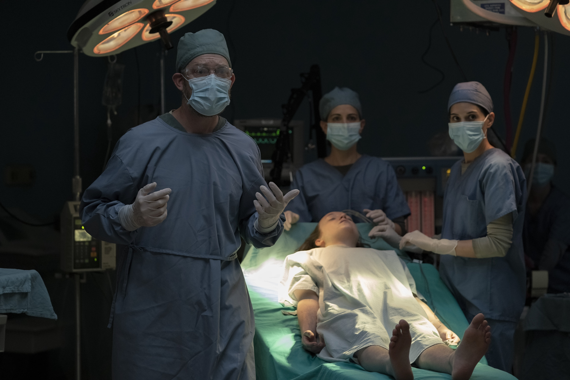 Men and women in scrubs and masks stand around a surgical table holding the unconscious Ellie (Bella Ramsey), about to euthanize her, in The Last of Us season 1, episode 9 Men and women in scrubs and masks stand around a surgical table holding the unconscious Ellie (Bella Ramsey), about to euthanize her, in The Last of Us season 1, episode 9