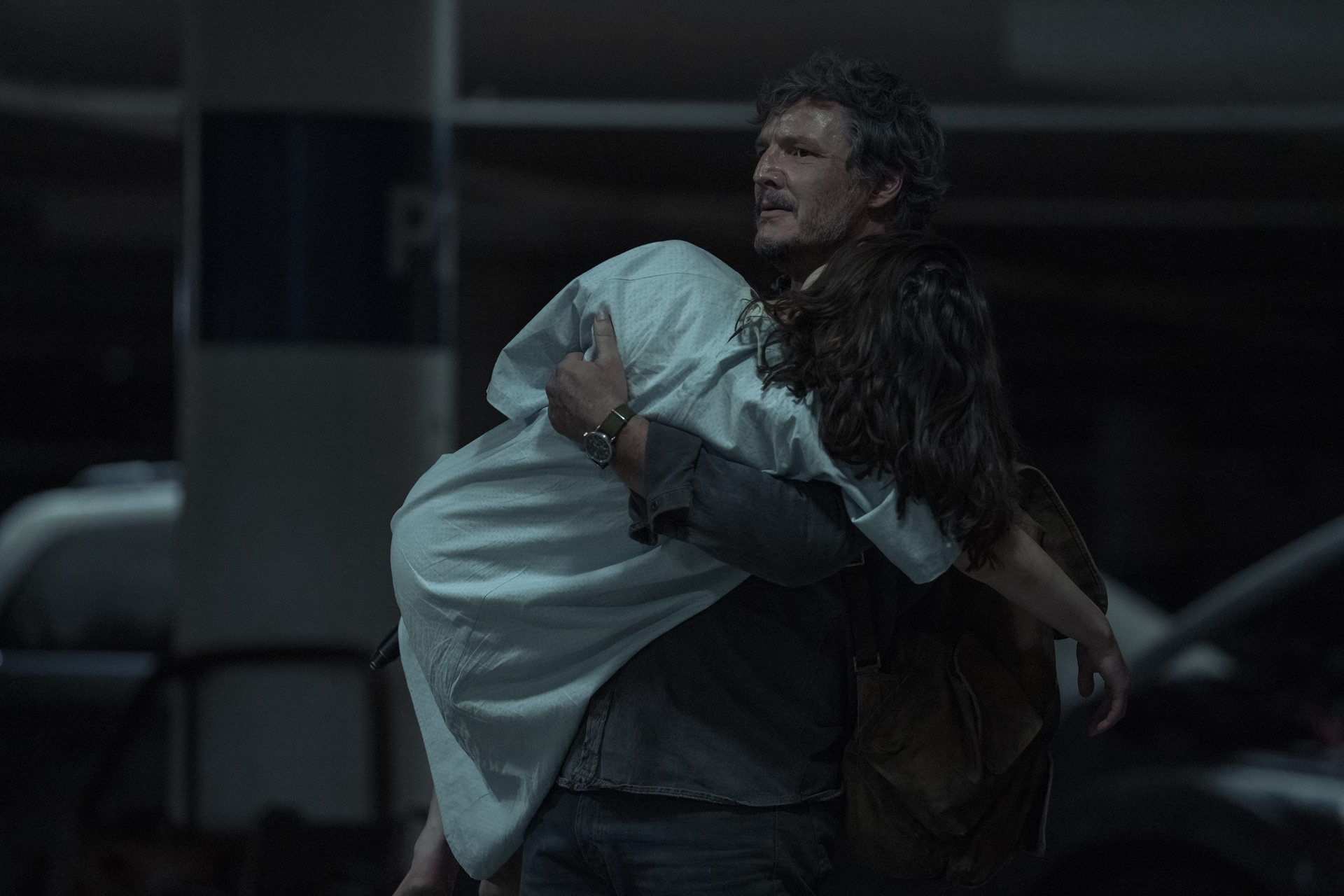Joel (Pedro Pascal) carries a limp, scrubs-clad Ellie (Bella Ramsey) as they escape from the Fireflies in The Last of Us season 1, episode 9 Joel (Pedro Pascal) carries a limp, scrubs-clad Ellie (Bella Ramsey) as they escape from the Fireflies in The Last of Us season 1, episode 9