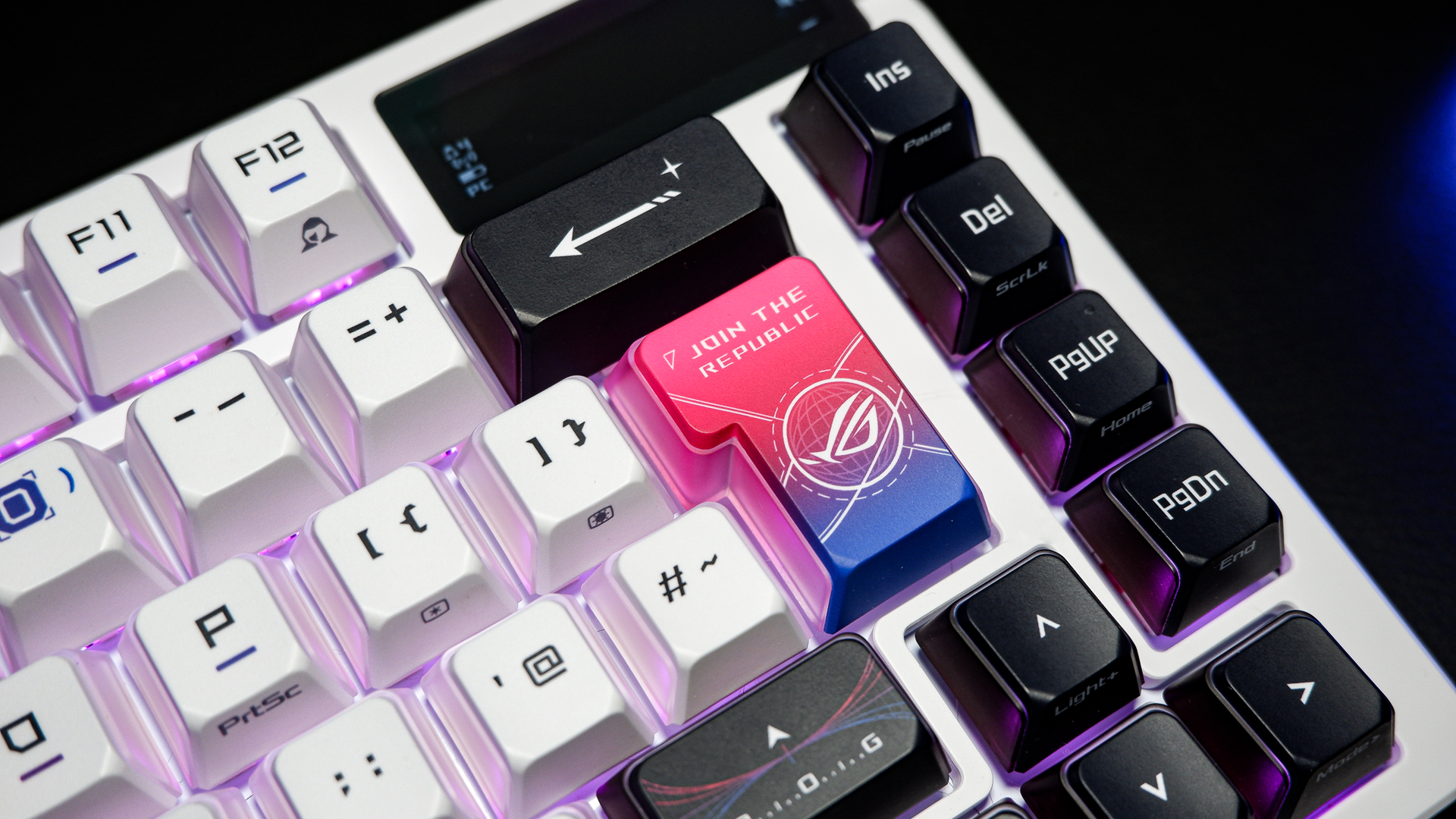 An Asus ROG Azoth X gaming keyboard on a desk with wrist rest and lighting enabled.