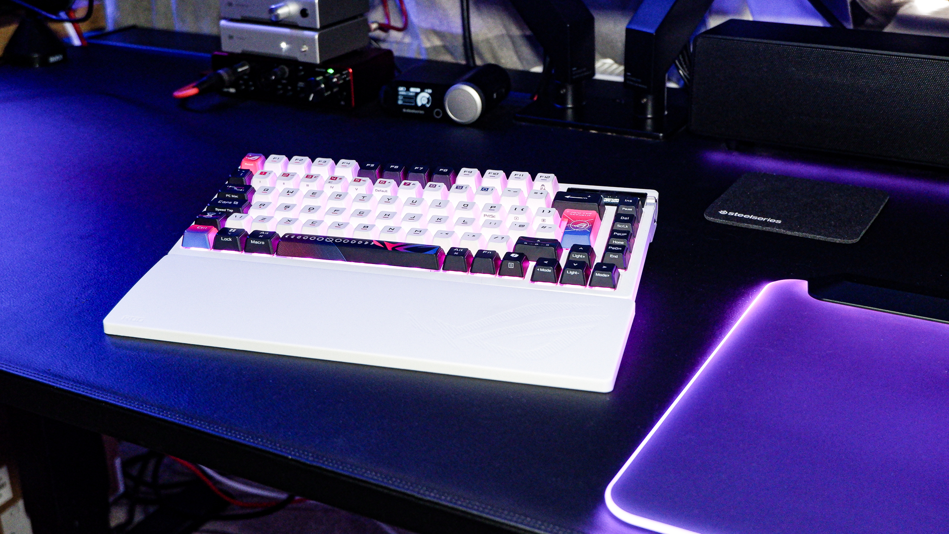 An Asus ROG Azoth X gaming keyboard on a desk with wrist rest and lighting enabled.