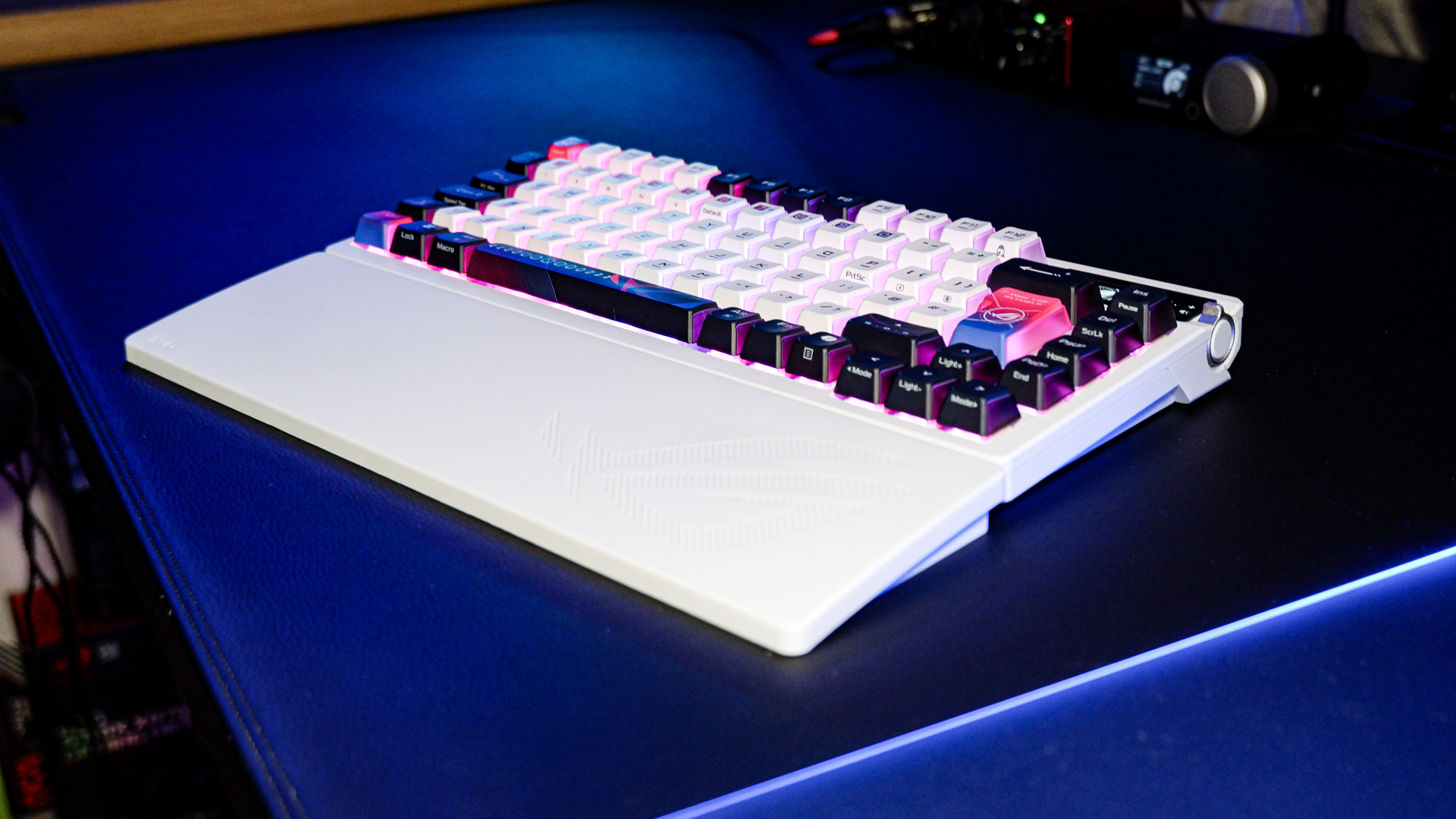 An Asus ROG Azoth X gaming keyboard on a desk with wrist rest and lighting enabled.