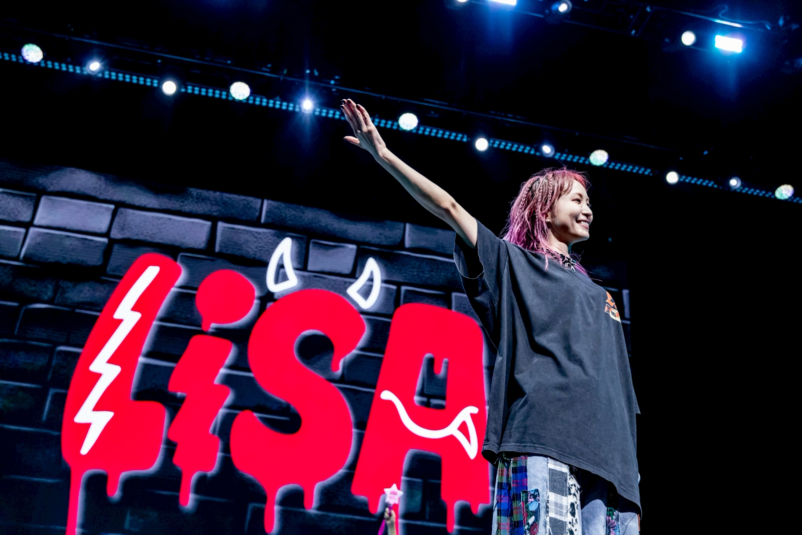 J-pop musician LiSA, on stage with a huge red sign featuring her name — with little devil horns on the “S” — in the background