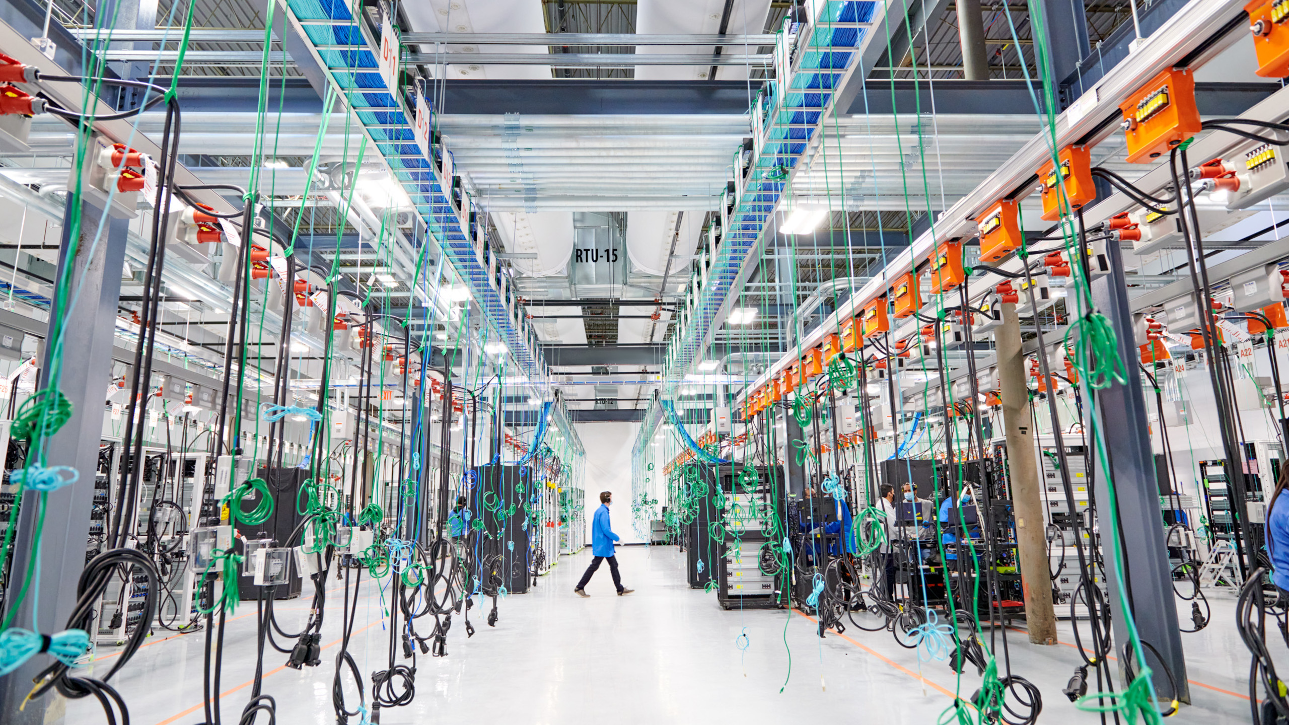 A photo of a large computer centre, showing clean white floors and many cables hanging from the ceiling
