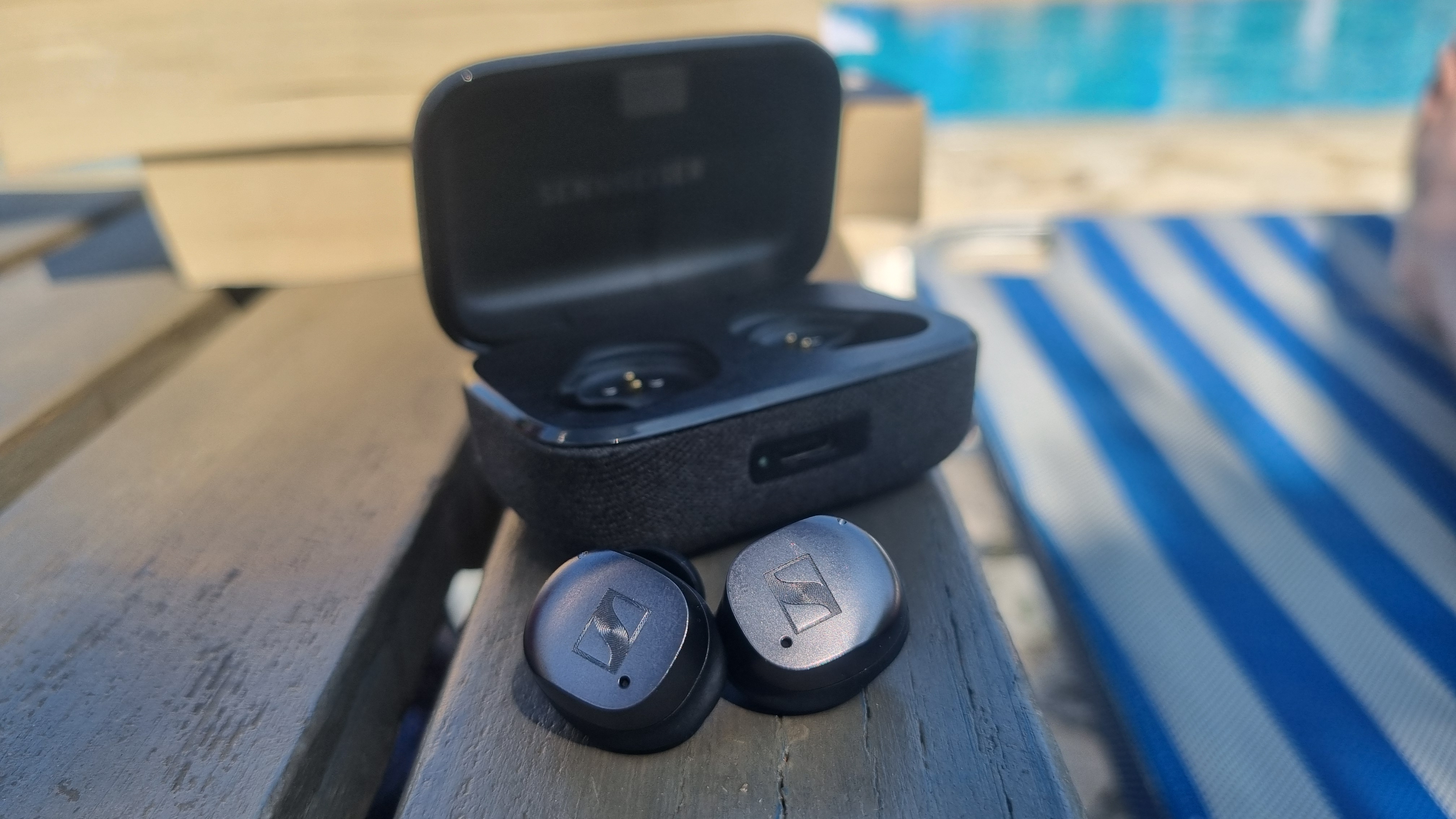 The Sennheiser Momentum True Wireless 4 earbuds outside of their case on a wooden bench