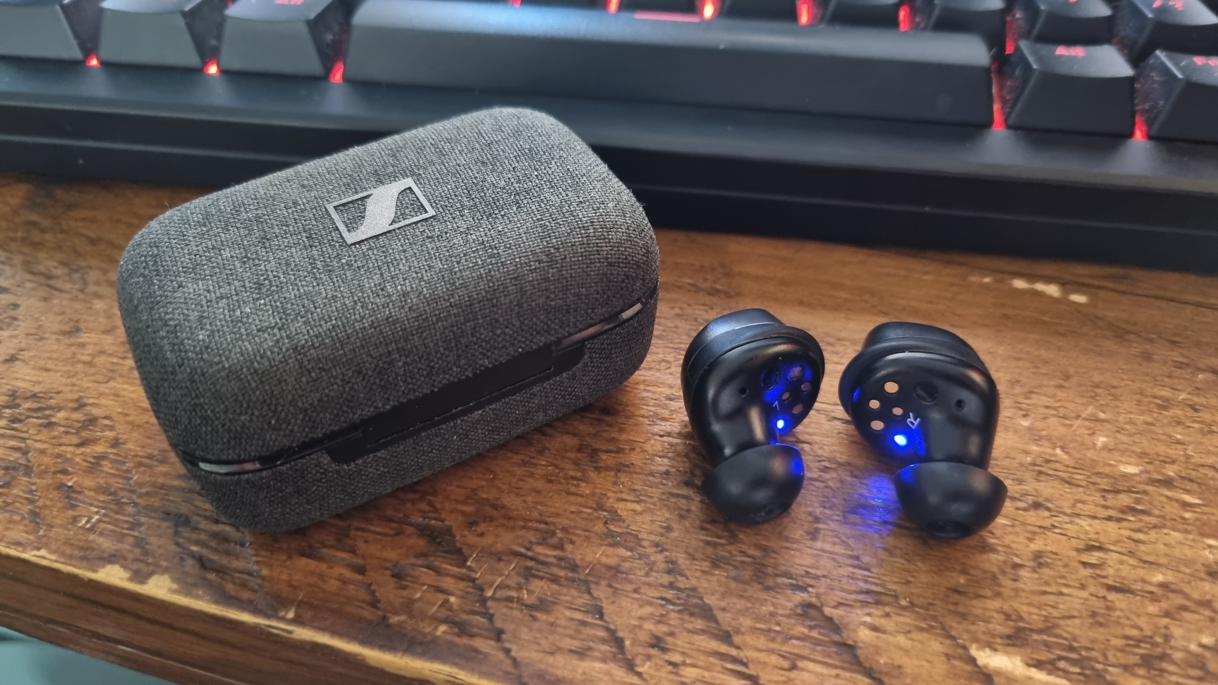 The Sennheiser Momentum True Wireless 4 earbuds next to their case, on a table