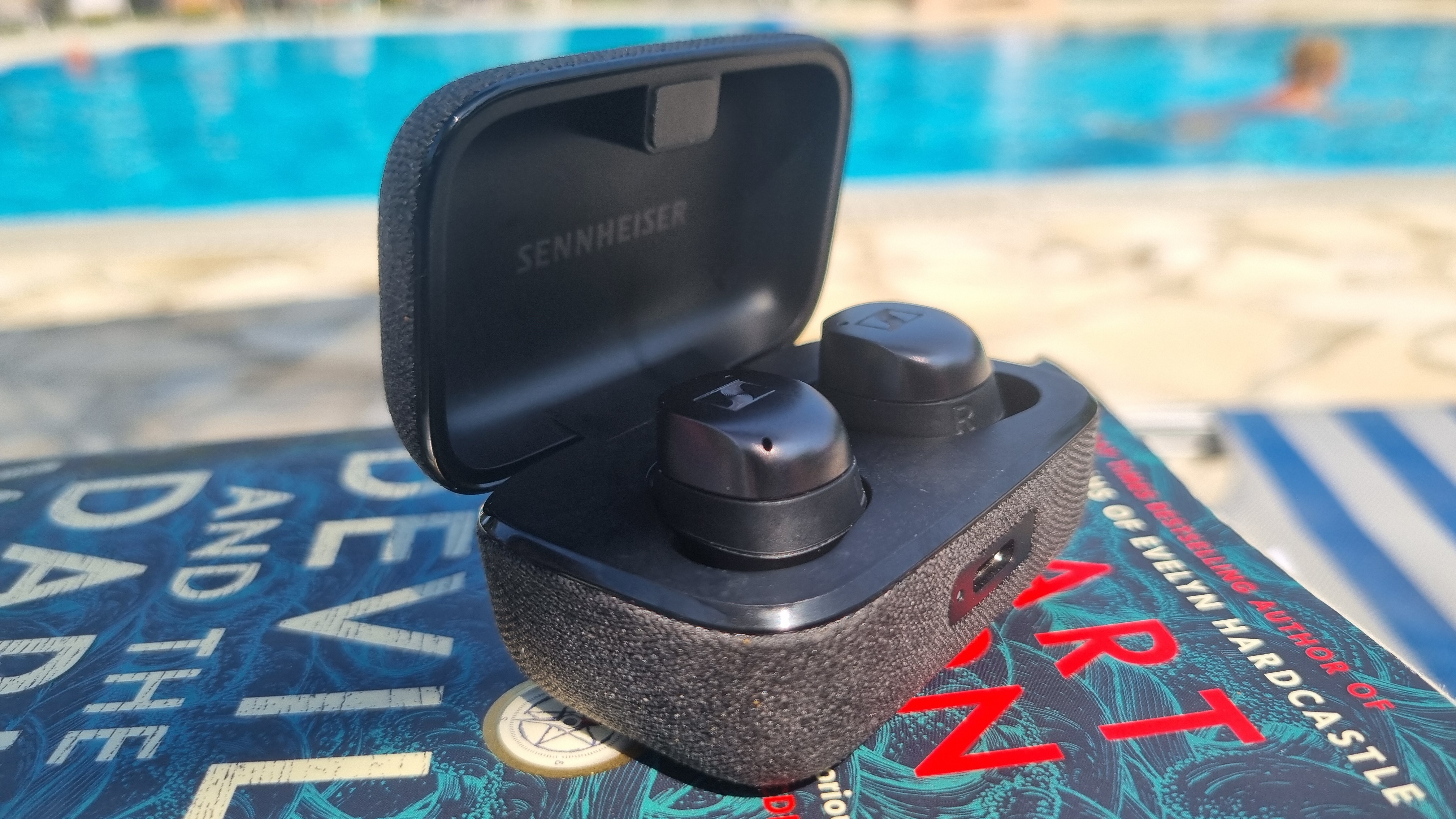 Sennheiser Momentum True Wireless 4 earbuds by the pool, on a book