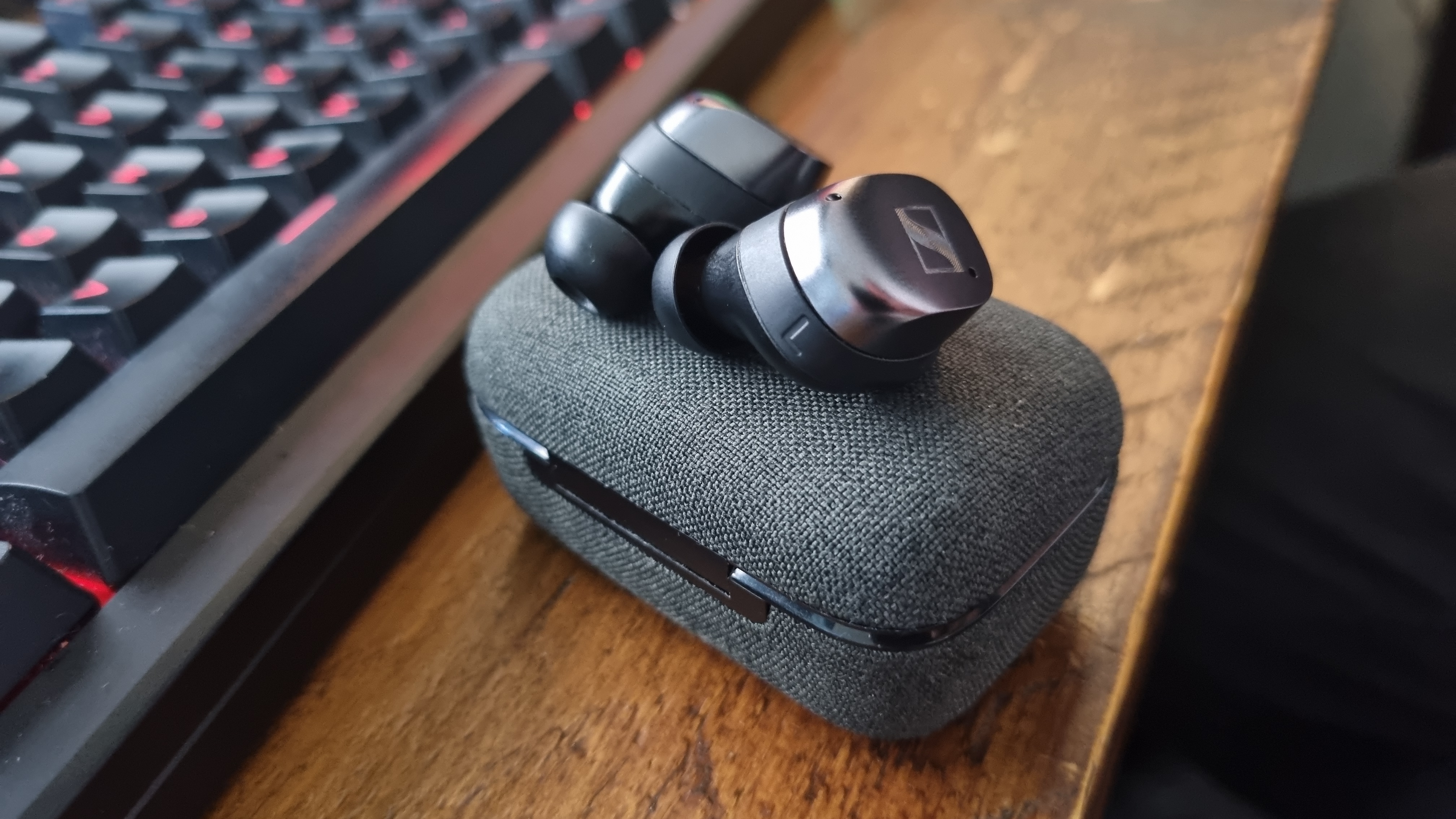 Two Sennheiser Momentum True Wireless 4 earbuds on top of their case next to a gaming keyboard