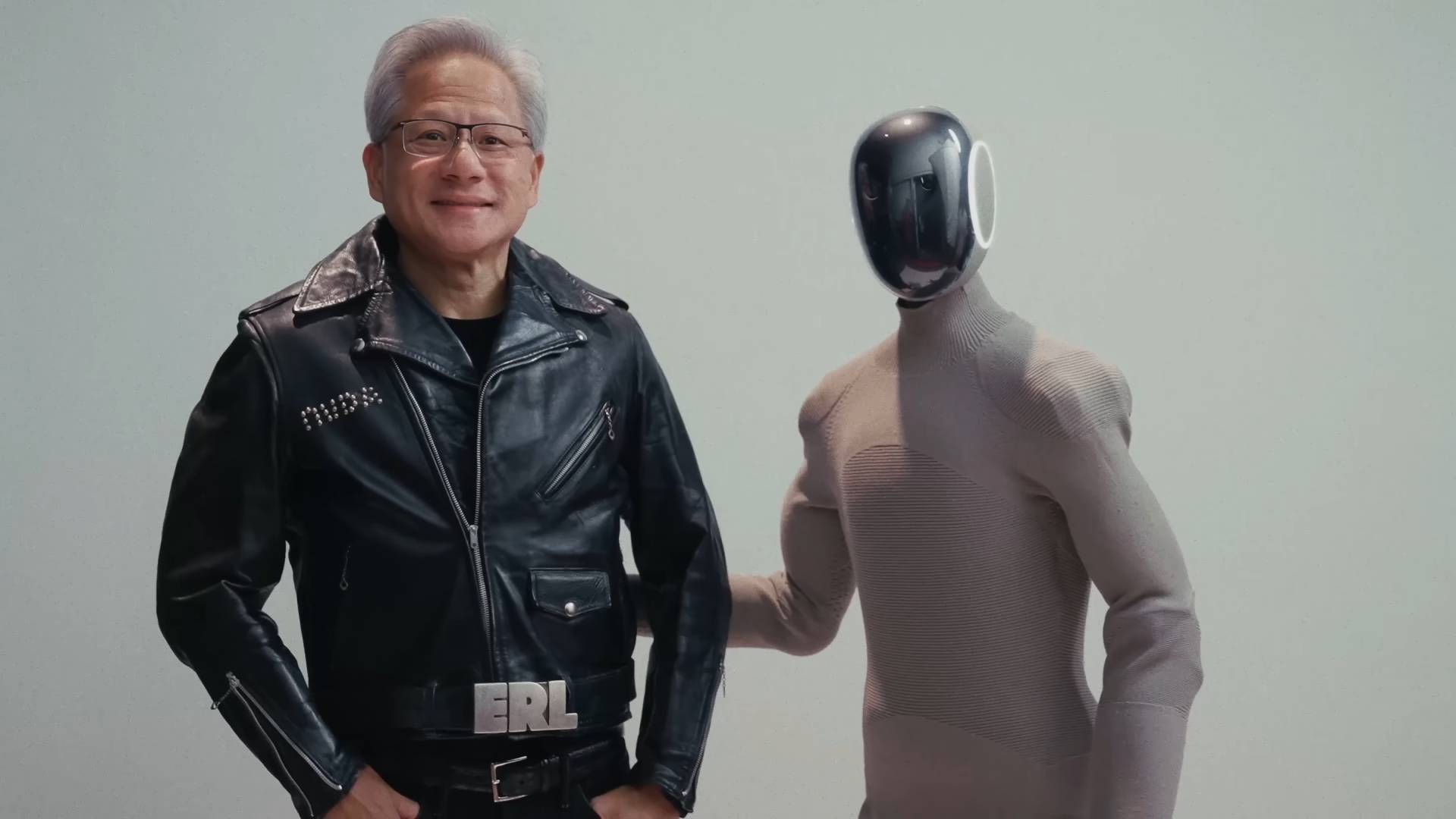 1X Technologies humanoid robot, the Neo Gamma, standing alongside Nvidia CEO Jensen Huang. Huang is wearing an ERL-made studded leather jacket.