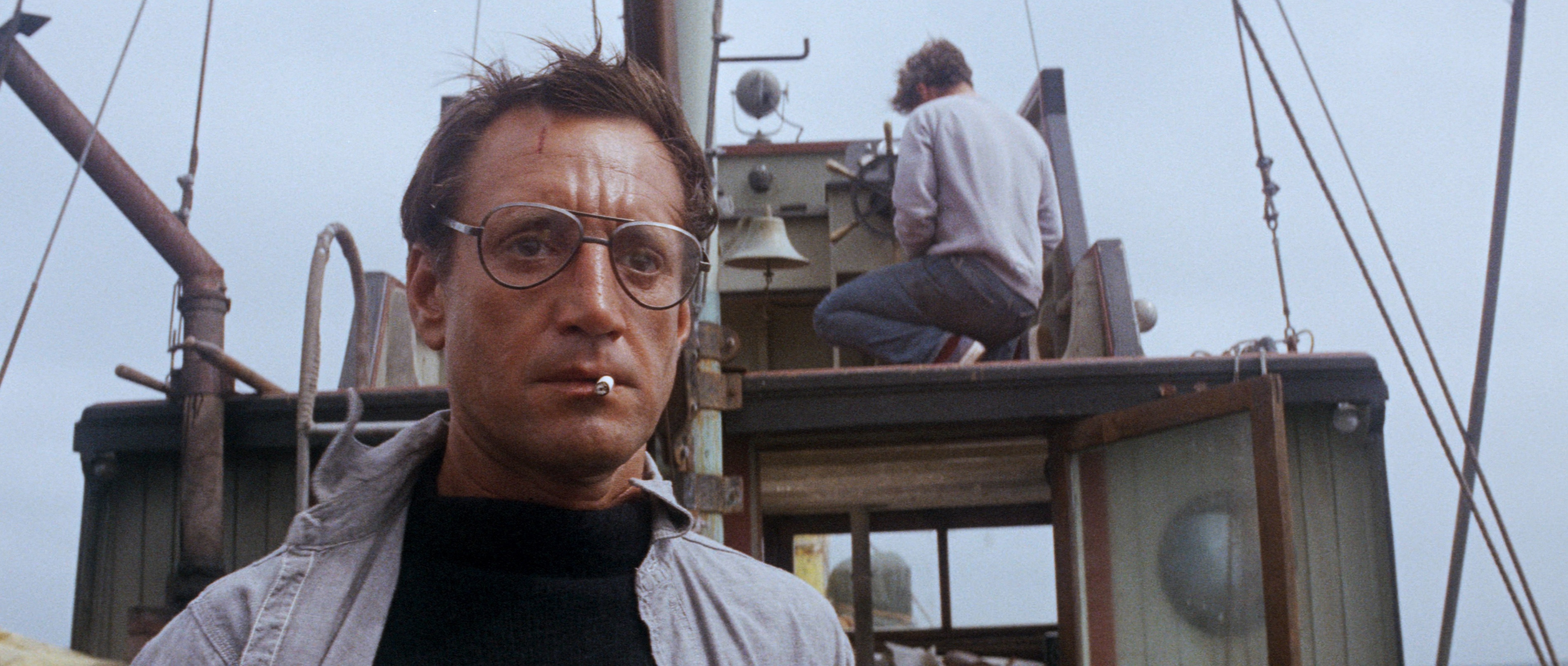 Roy Scheider as Police Chief Brody wearing big glasses and smoking a cigarette, stares in shock at the back end of a boat in Jaws Roy Scheider as Police Chief Brody wearing big glasses and smoking a cigarette, stares in shock at the back end of a boat in Jaws
