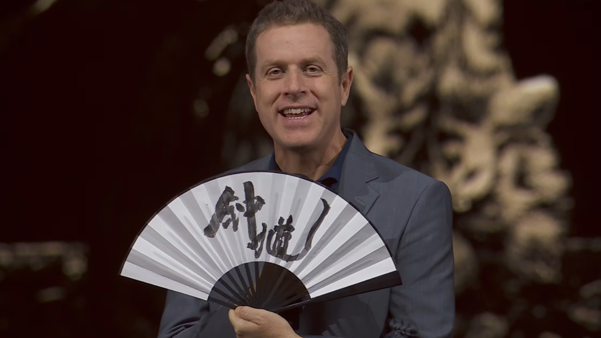 Geoff Keighley celebrating the reveal of Black Myth: Zhong Kui with an unfolded fan at Gamescom Opening Night Live 2025.