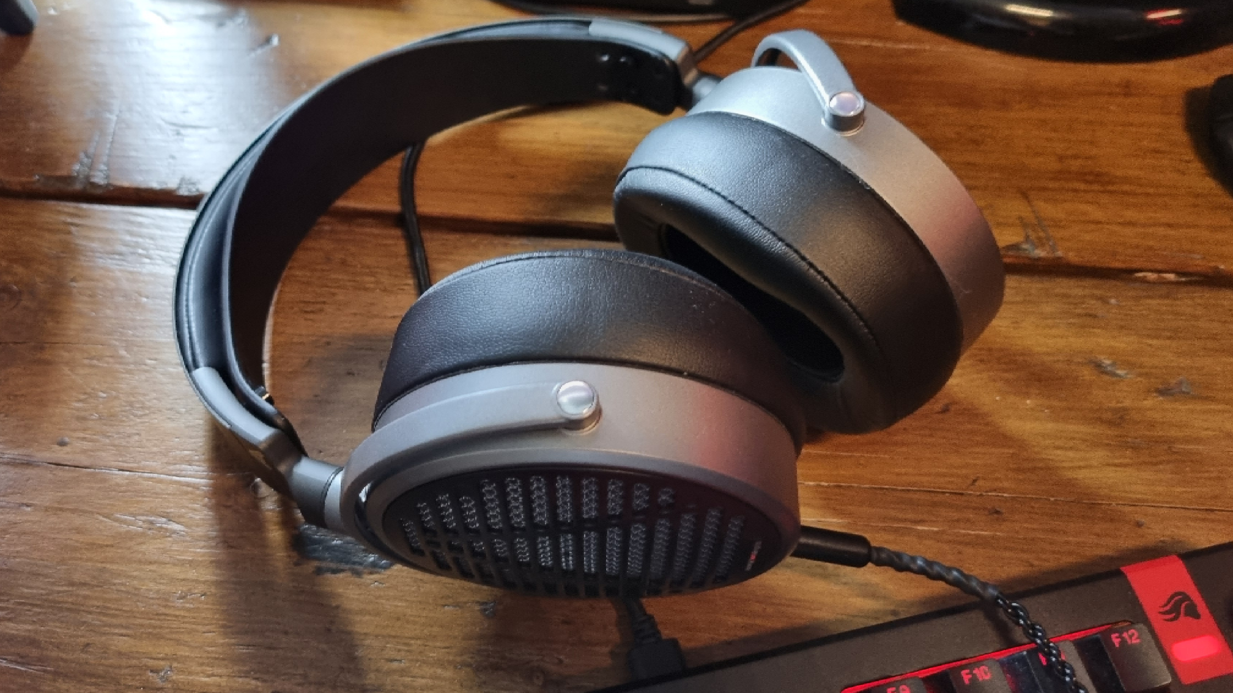 The Audeze MM-100 headphones on a wooden desk, above a gaming keyboard