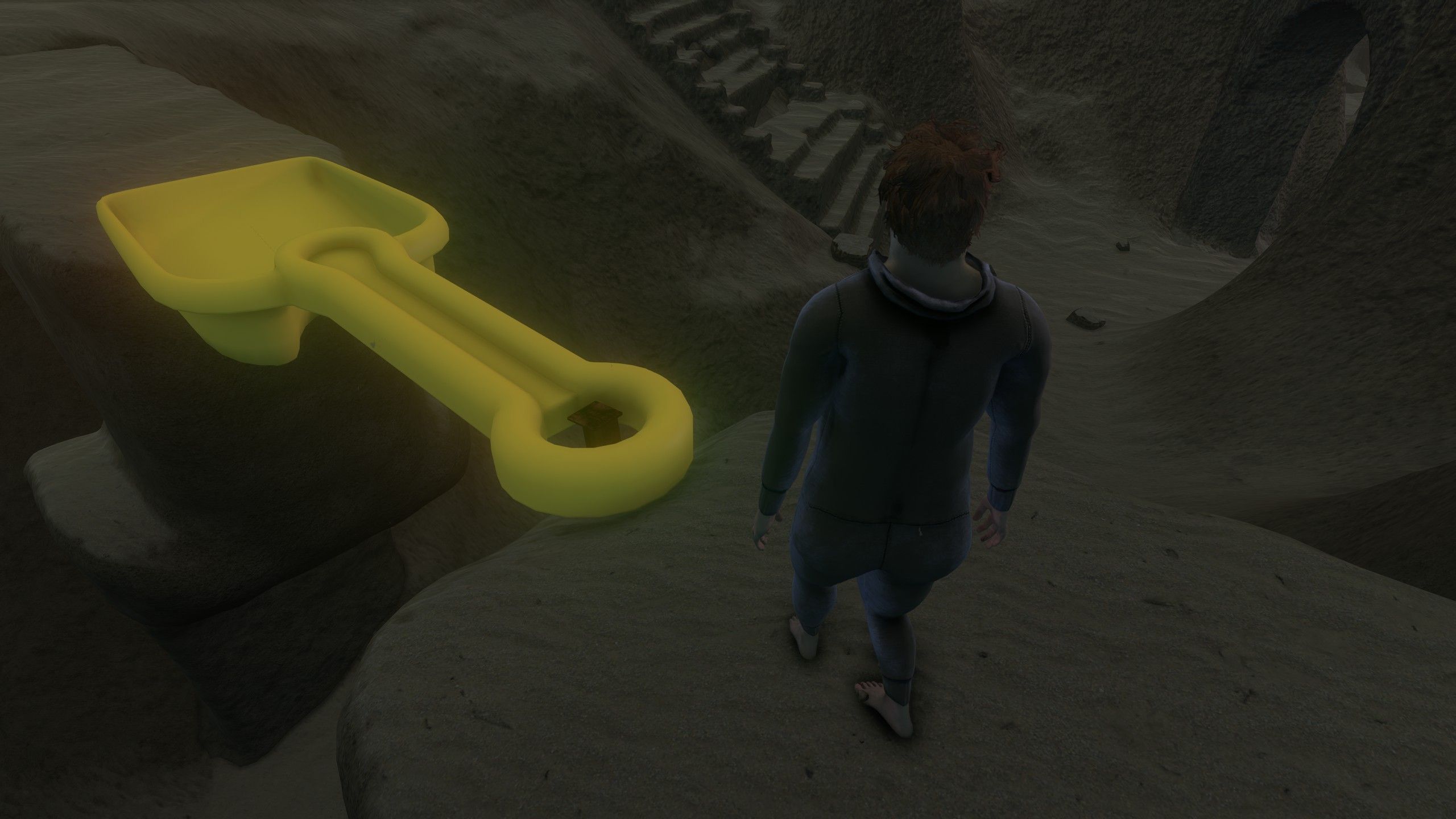 A yellow plastic shovel forms a bridge between two sandy ledges