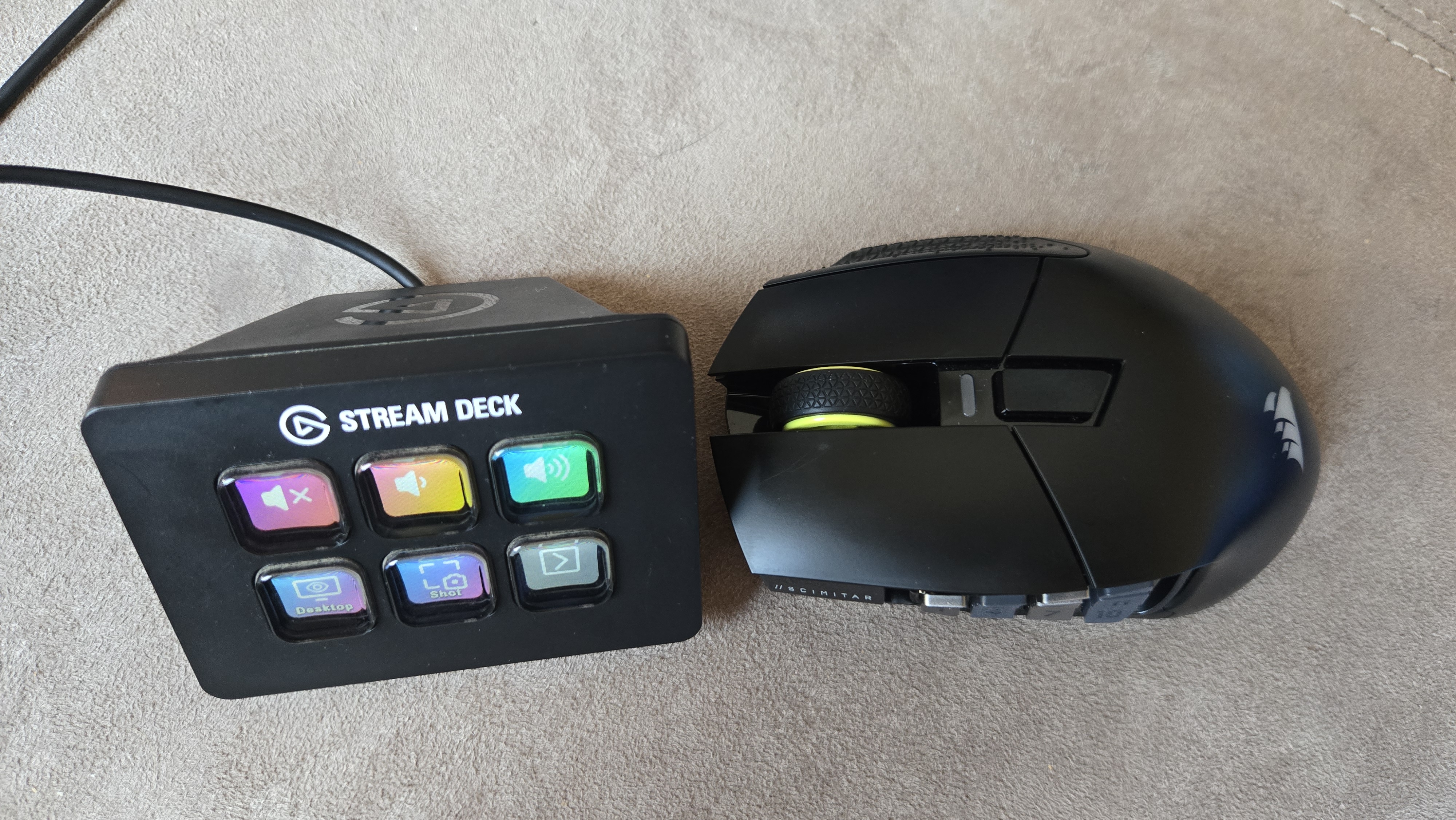A Corsair Scimitar Elite Wireless SE gaming mouse on a carpet next to a gaming laptop and Stream Deck.