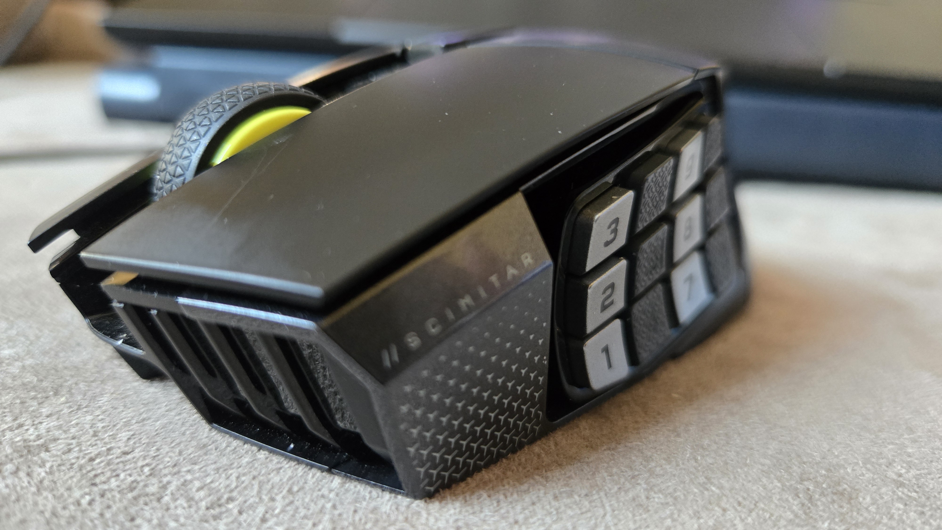 A Corsair Scimitar Elite Wireless SE gaming mouse on a carpet next to a gaming laptop and Stream Deck.