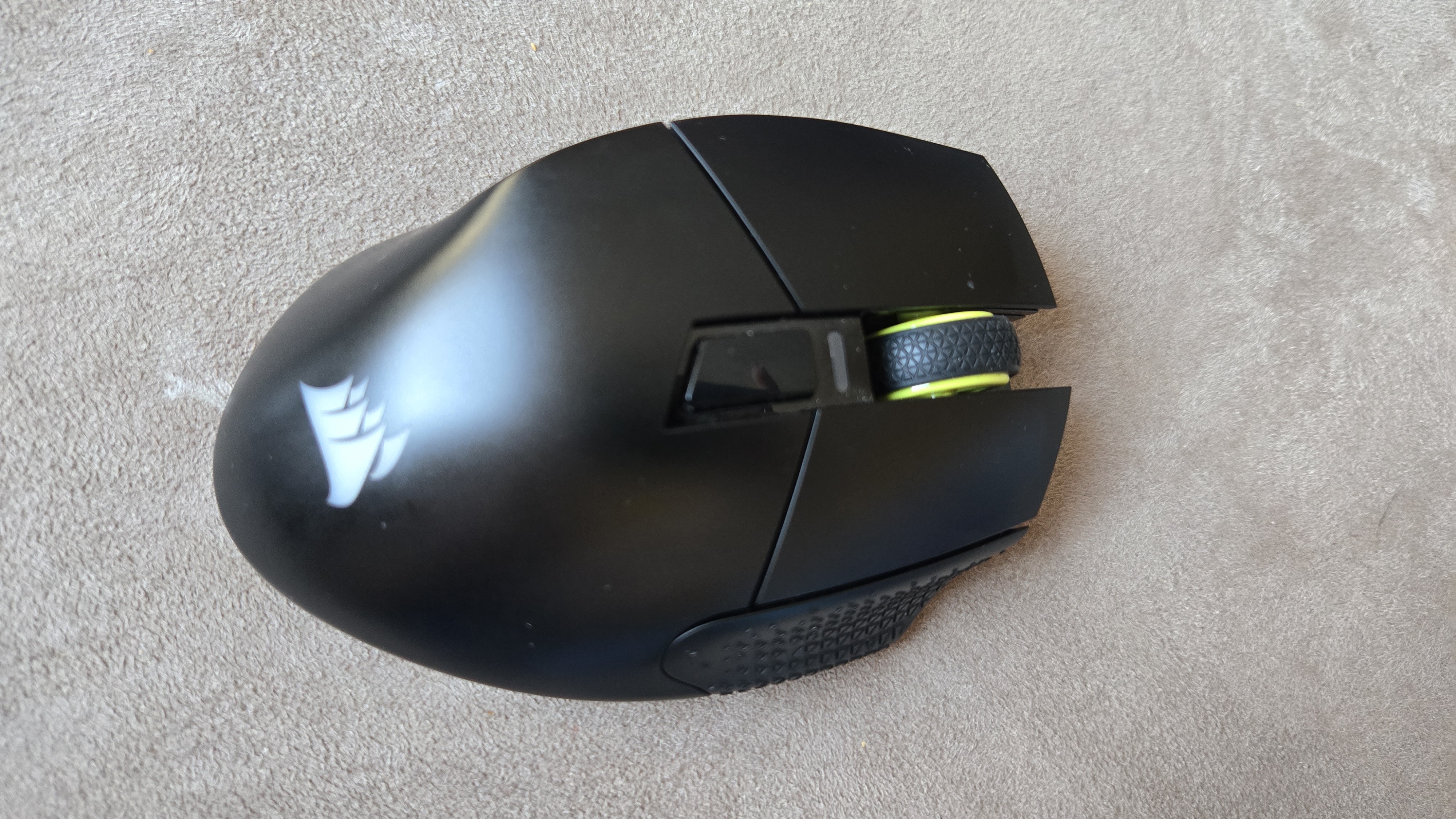 A Corsair Scimitar Elite Wireless SE gaming mouse on a carpet next to a gaming laptop and Stream Deck.