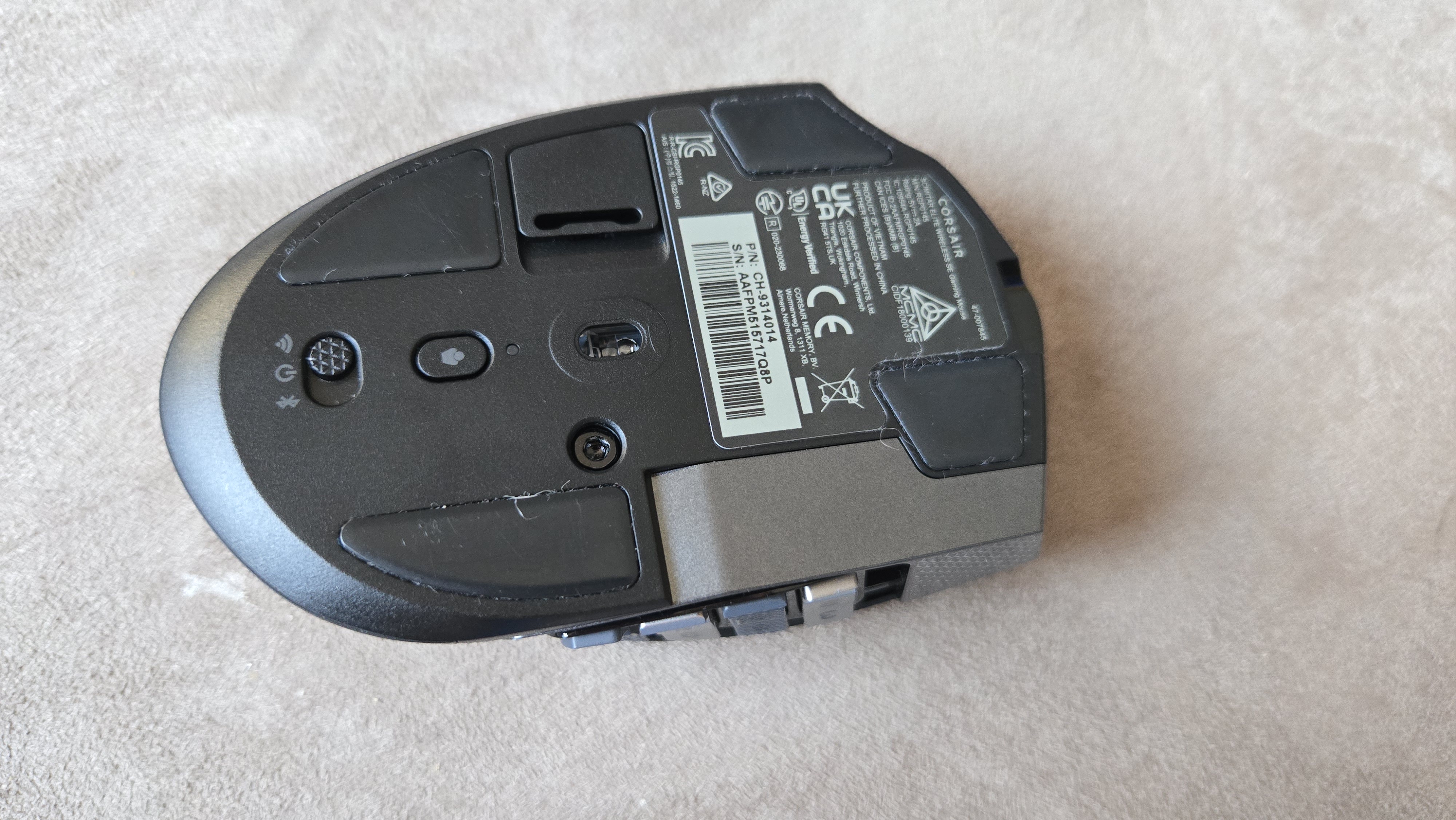 A Corsair Scimitar Elite Wireless SE gaming mouse on a carpet next to a gaming laptop and Stream Deck.