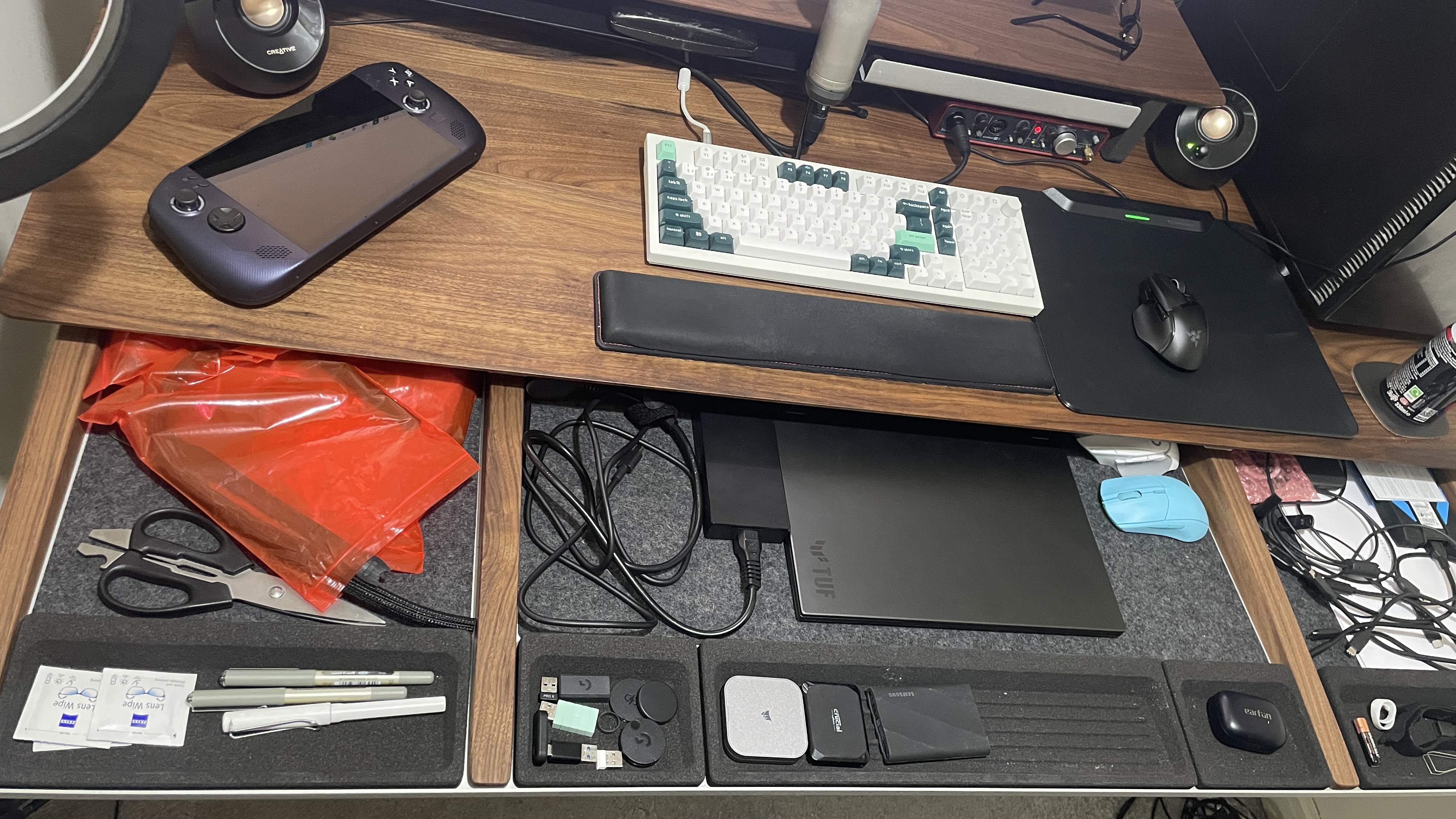 A walnut Grovemade desk with its draw open, showing devices and stationery inside