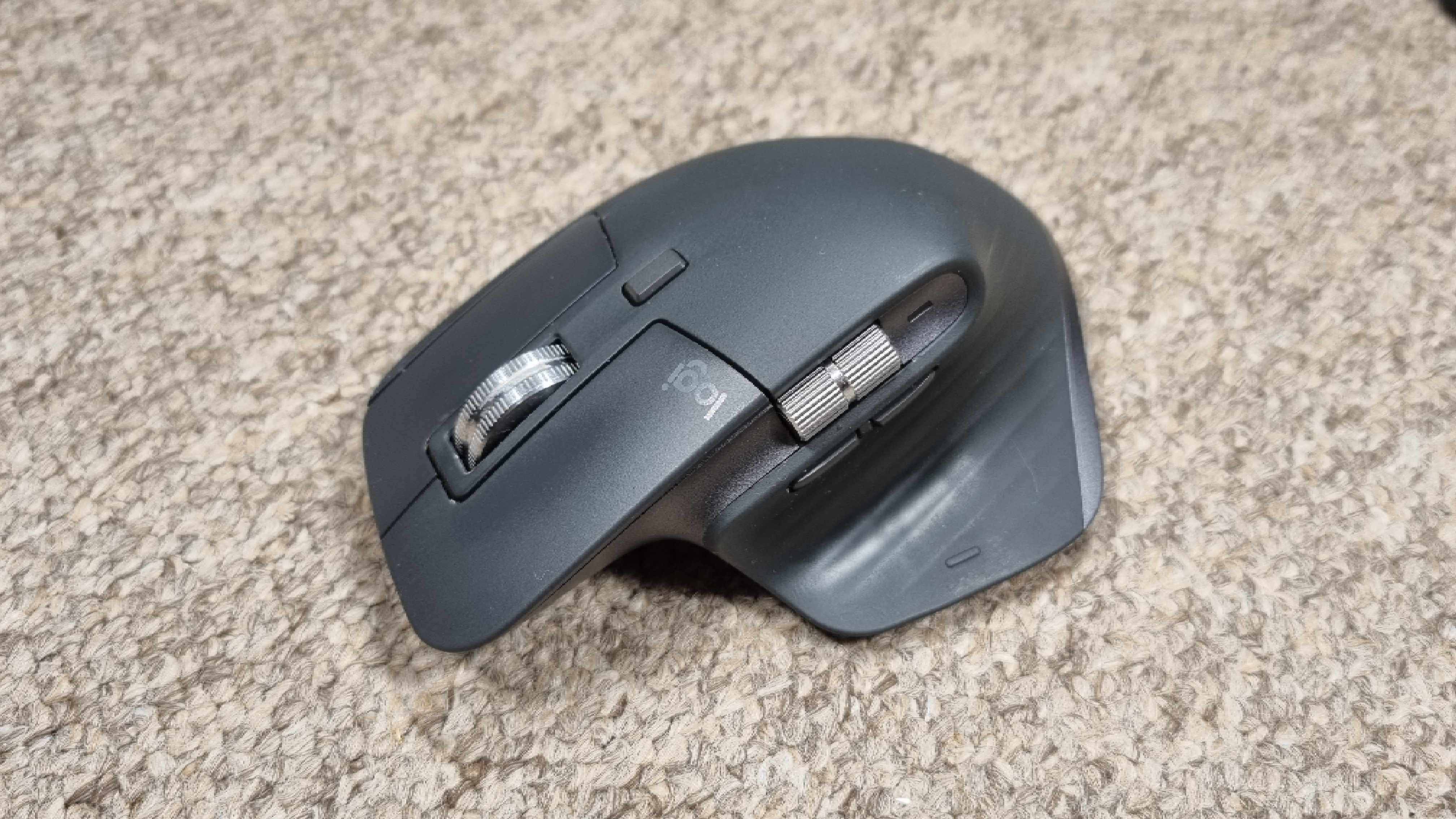 A Logitech MX Master 3S mouse on carpet, with an orange light above it