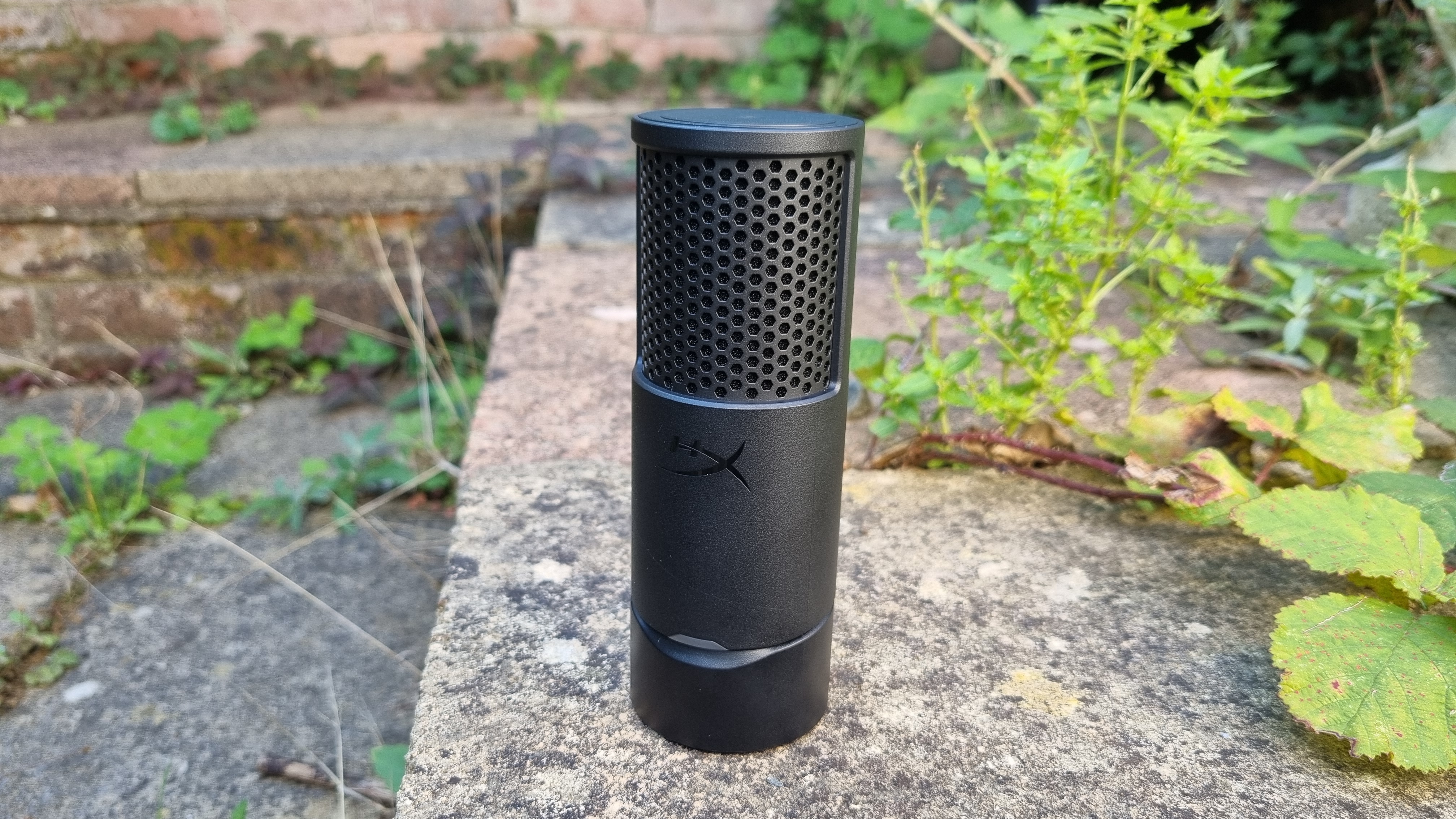 The HyperX SoloCast 2 USB microphone stood on its end, outside among some foliage