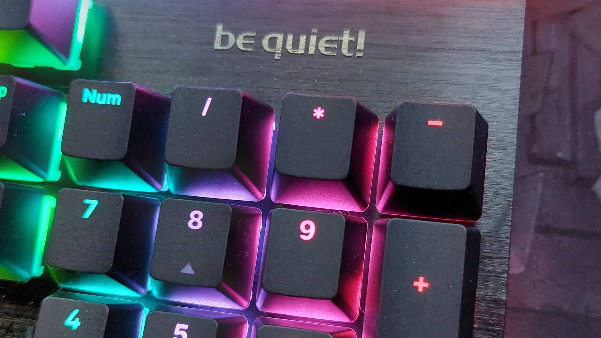 A close up of the Be Quiet Light Mount gaming mechanical keyboard. Above the numberpad, we can see the 'be quiet!' logo with letters in shiny metal. The keyboard's RGB light are on.