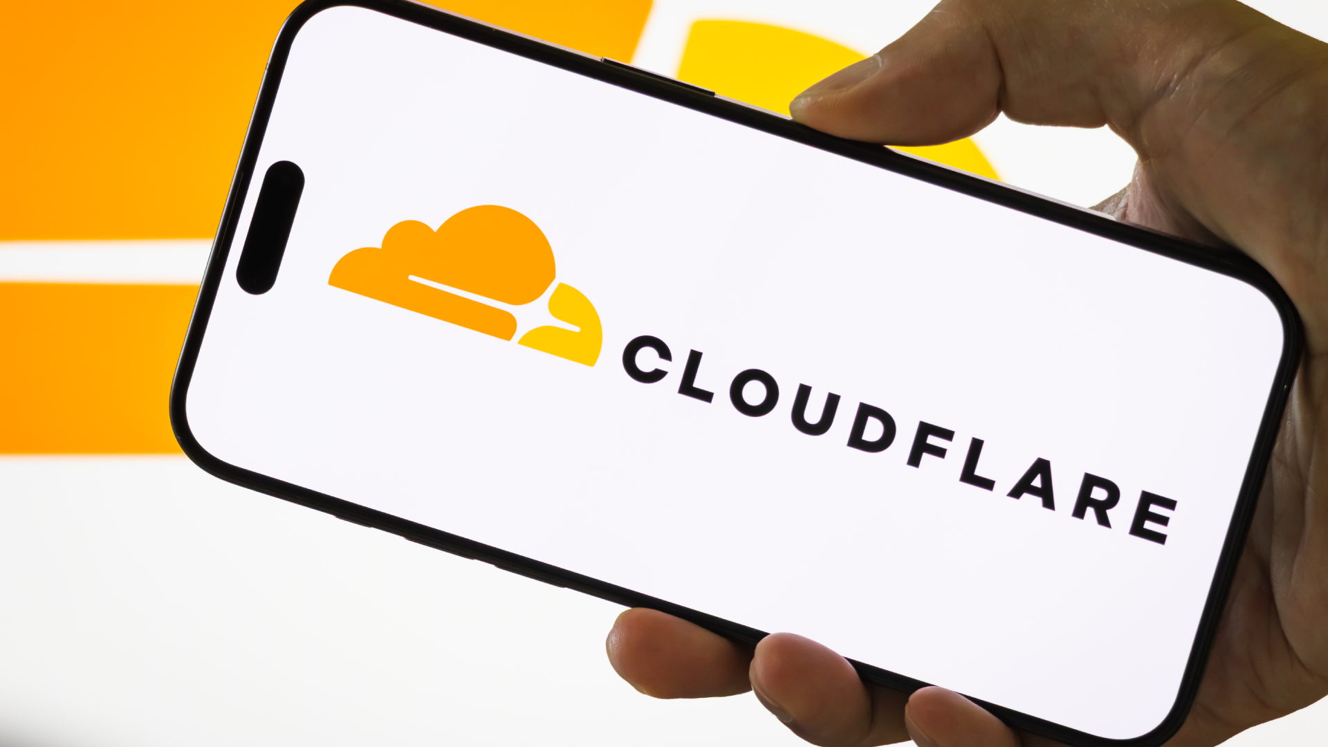 CHONGQING, CHINA - JULY 29: In this photo illustration, a person holds a smartphone displaying the logo of Cloudflare Inc. (NYSE: NET), an American web infrastructure and website security company, with the company's cloud logo visible in the background, on July 29, 2025 in Chongqing, China. (Photo illustration by Cheng Xin/Getty Images)