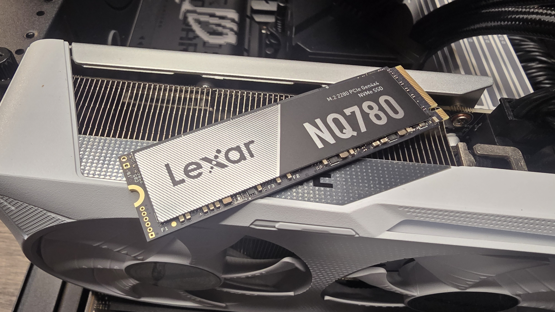 A Lexar NQ780 SSD installed inside a gaming PC and on top of a graphics card.