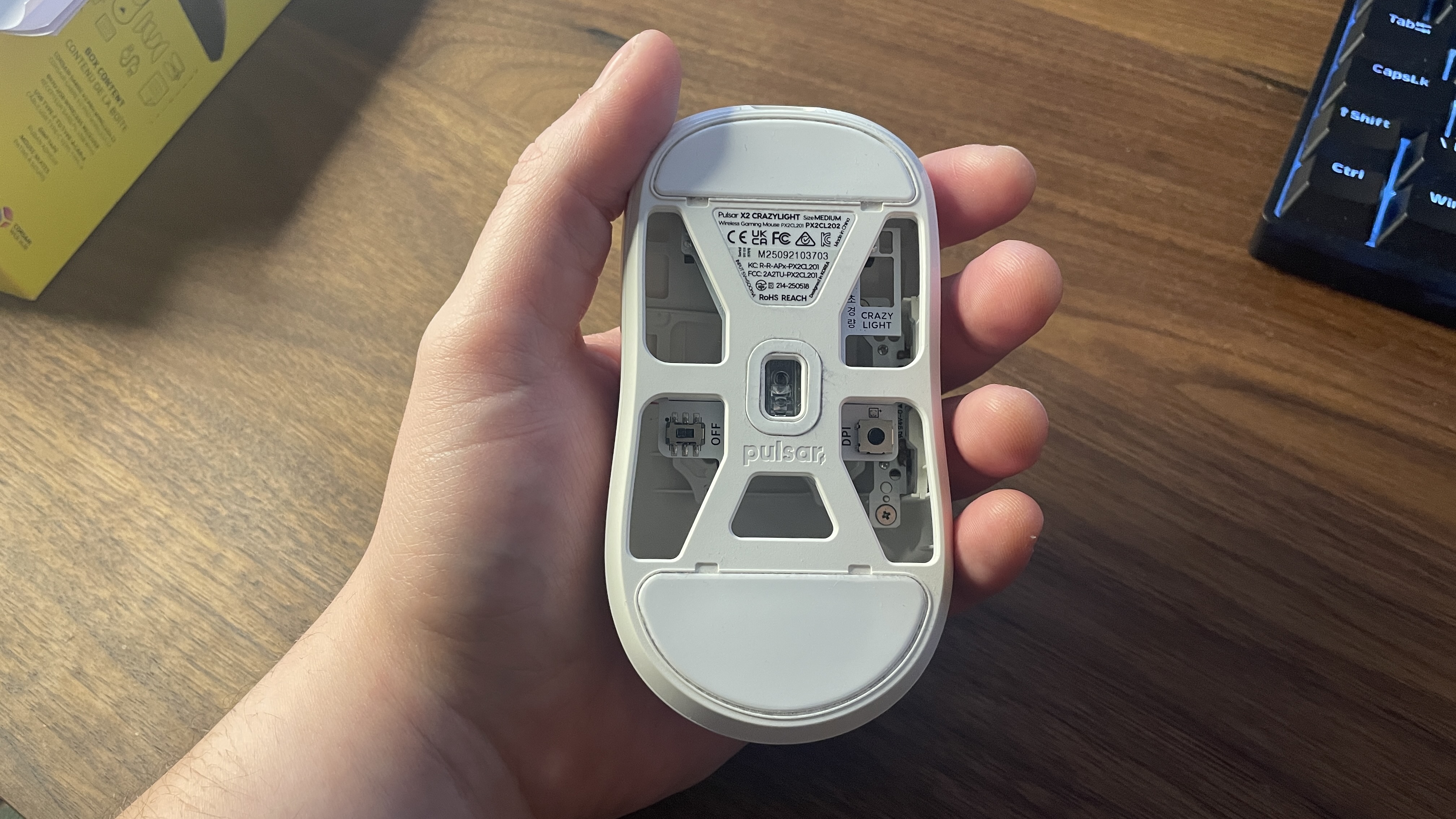 A Pulsar X2 CrazyLight gaming mouse in-hand, upside down, showing the holes in its underside.