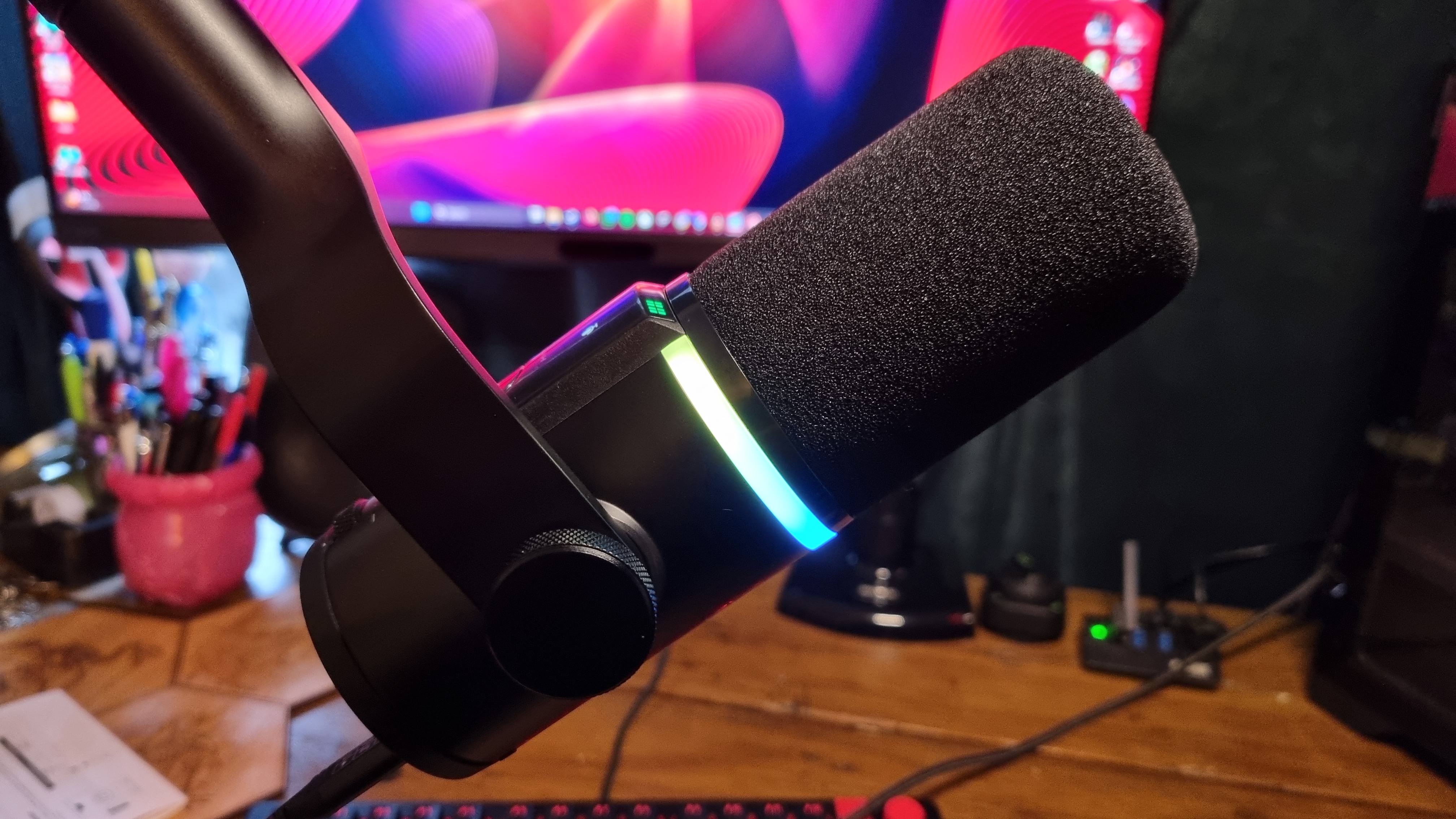 The HyperX FlipCast gaming microphone attached to a boom arm and shot from the side, with its RGB lit in blue and green