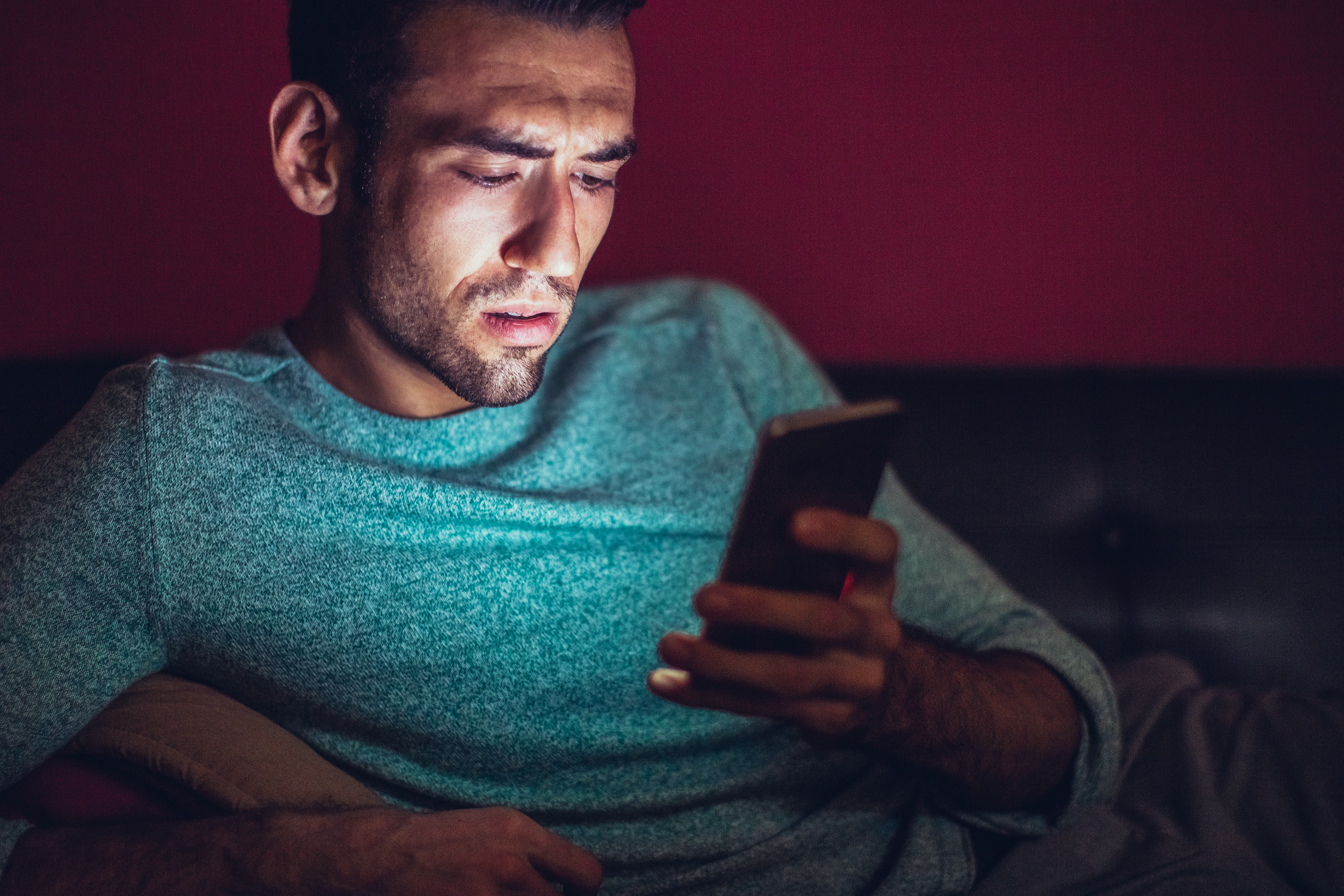 A man looking at a smartphone with a furrowed brow while sitting on a sofa.