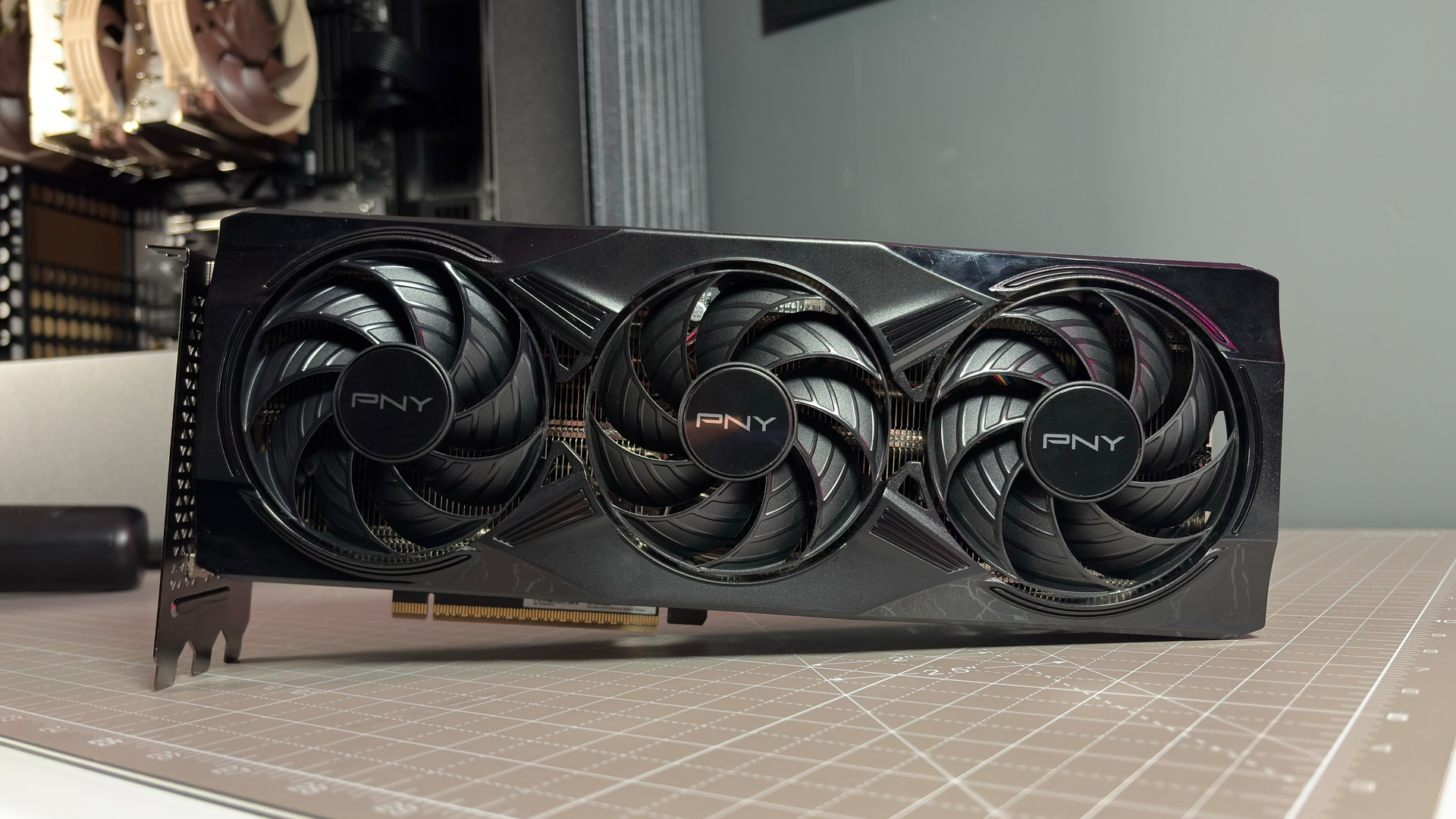 A PNY RTX 5070 Ti OC graphics card on a desk with a desk mat and pink light.