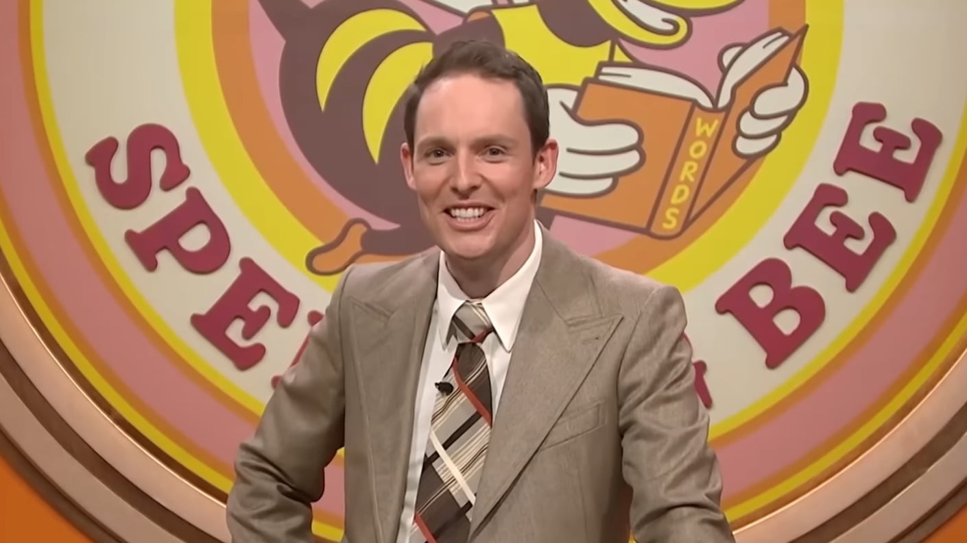 A still from Guy Montgomery's Guy Mont-Spelling Bee showing Guy Montgomery smiling at his podium