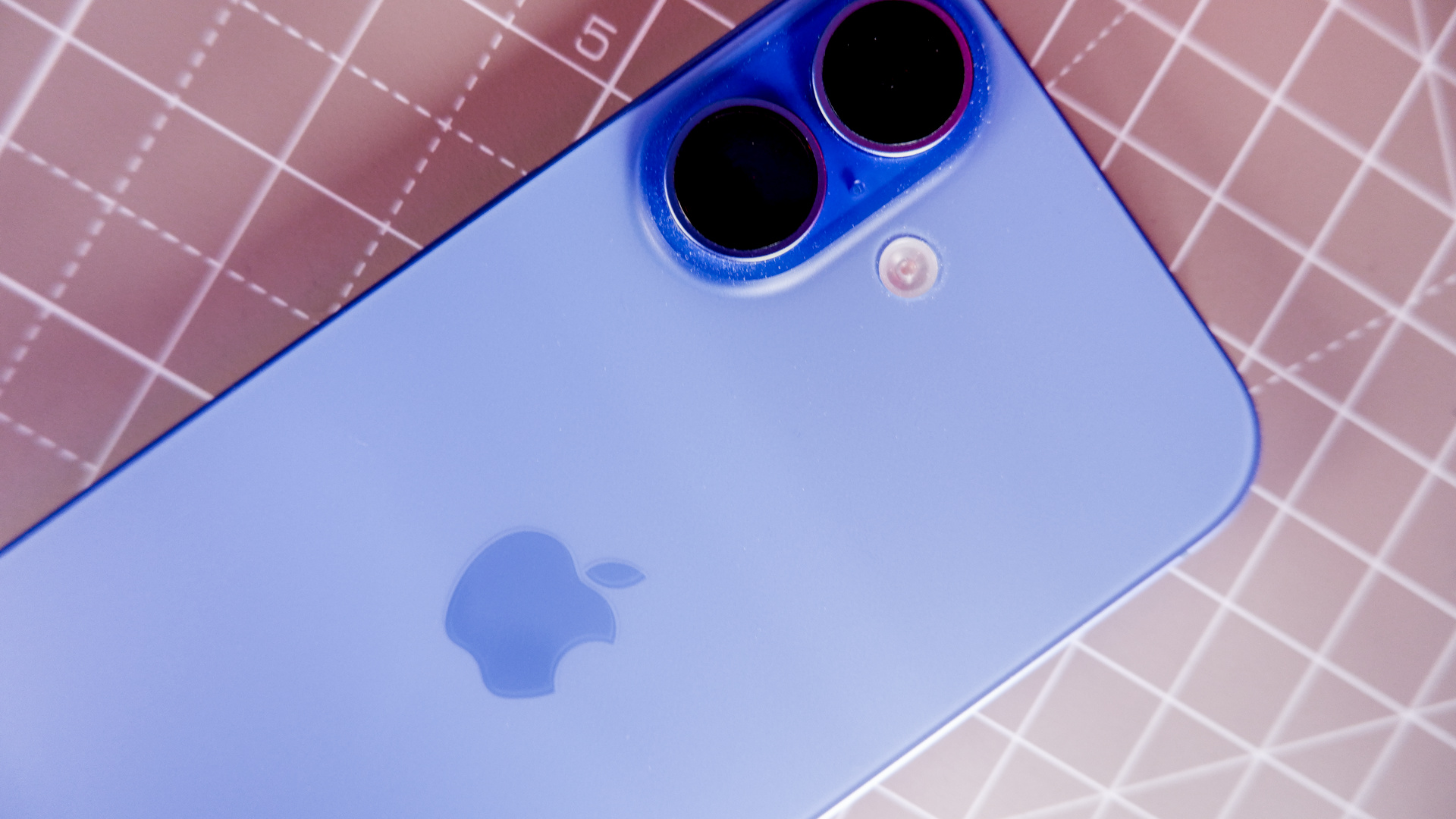 An iPad Mini A17 and iPhone 16 on a desk with a gaming PC in the background.