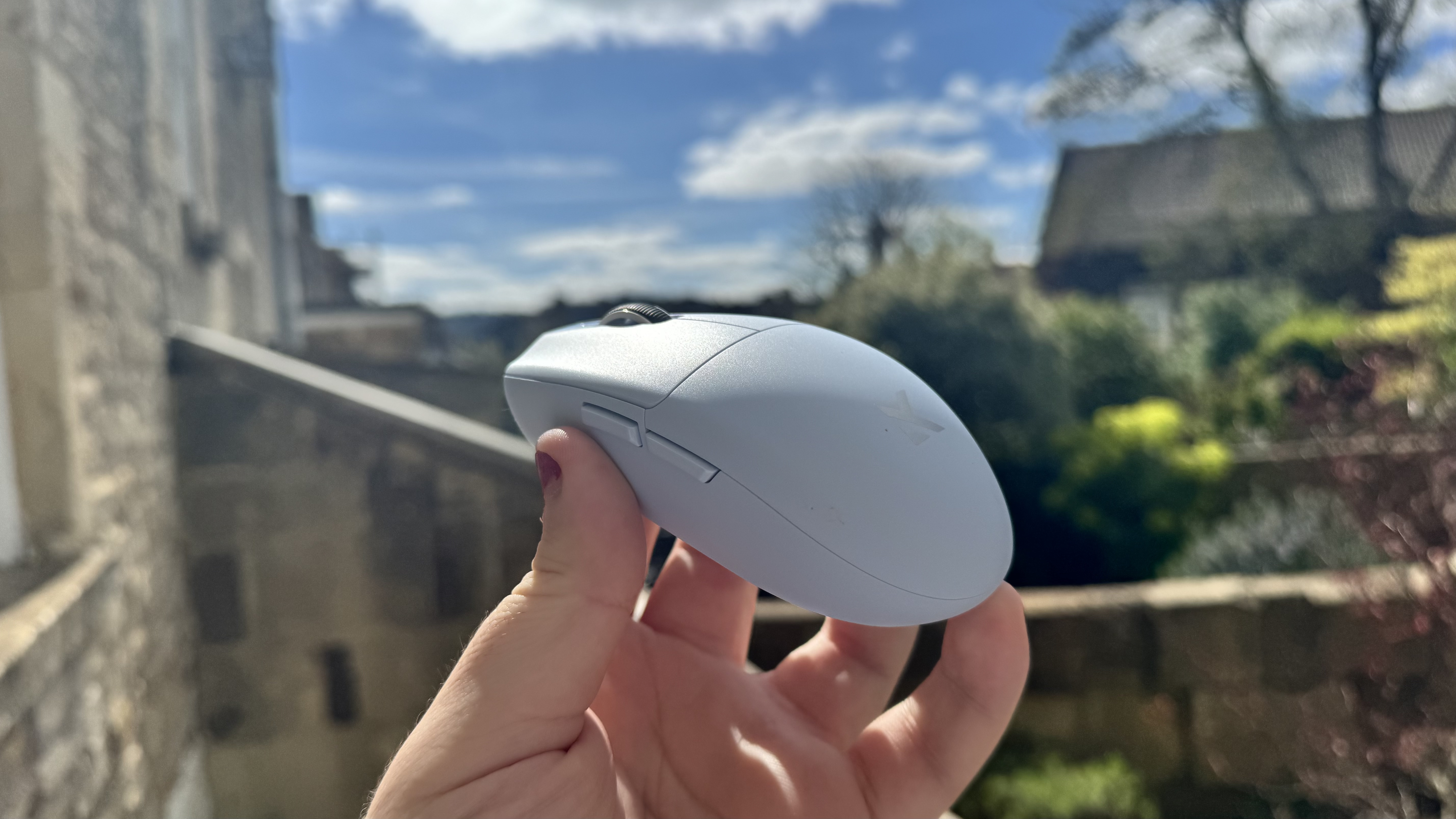 The blue Mchose G3 V2 gaming mouse from the side, in a hand in a garden