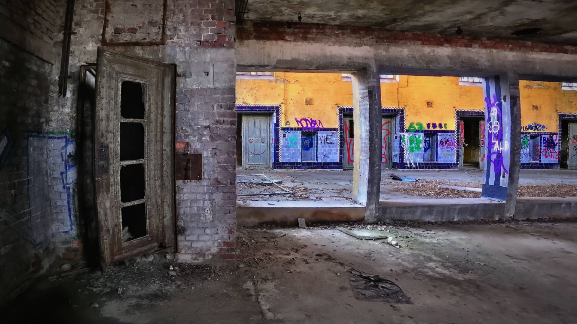 Part of a gaussian splat captured by scan artist Christoph Schindelar. This is an abandoned factory with crumbling, graffiti-lined walls. Doors can be seen in front of and behind a partitioning wall.