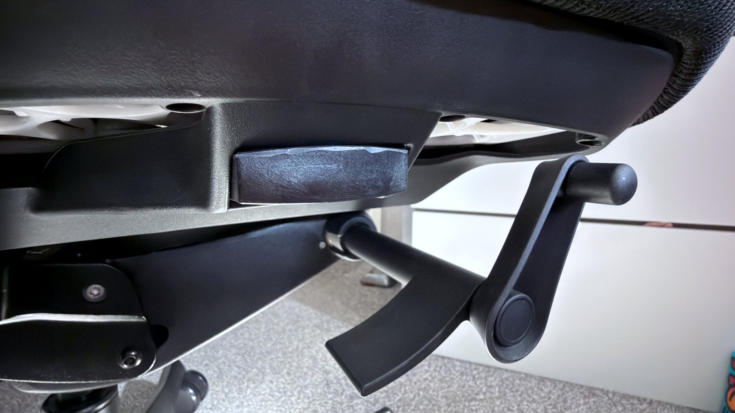 A photo of an Autonomous ErgoChair Ultra 2, showing a close-up view of the tension wheel for the back recline mechanism and latch to adjust the seat height