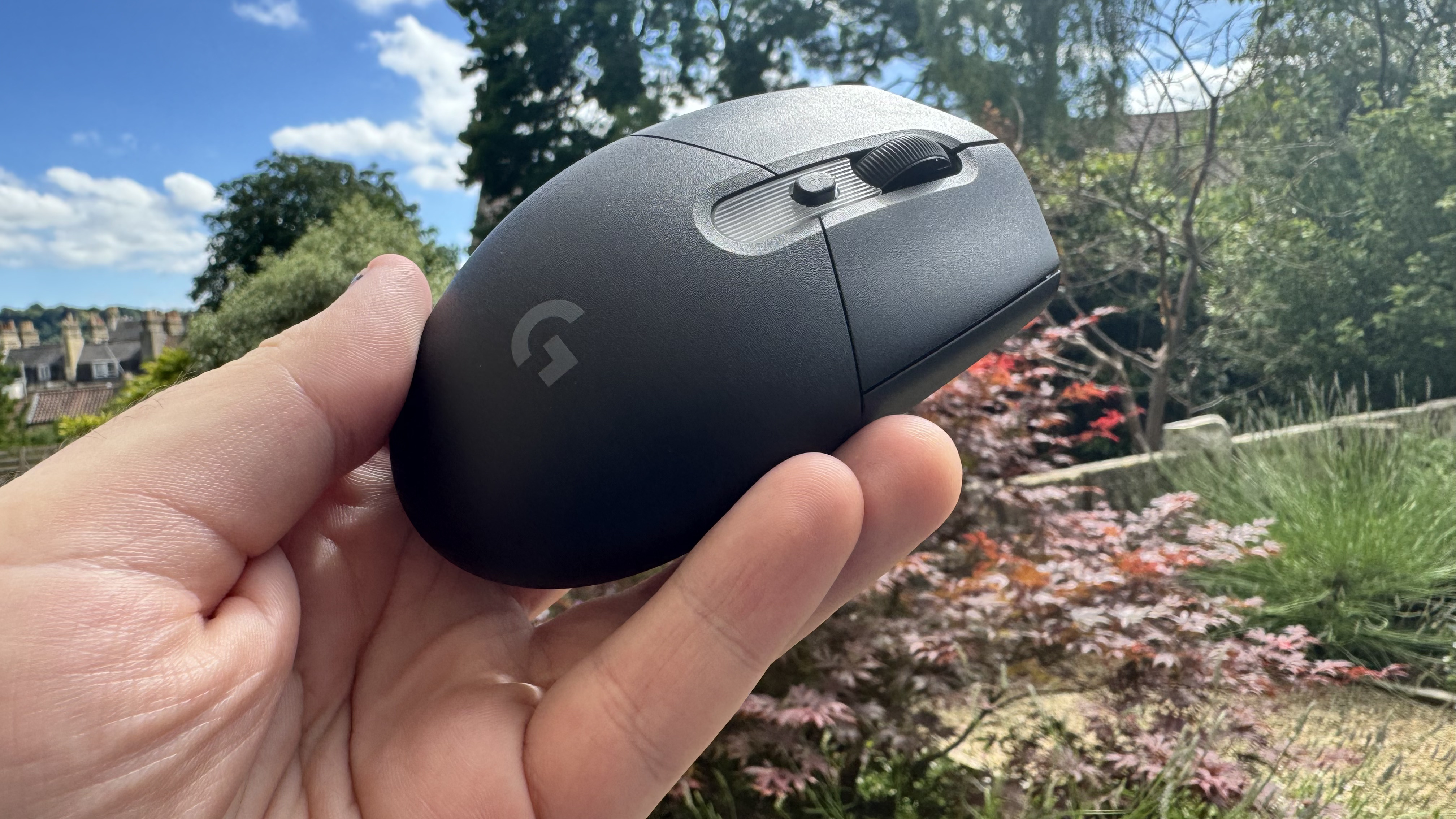 Logitech G305 X Superlight gaming mouse, held in a hand outside
