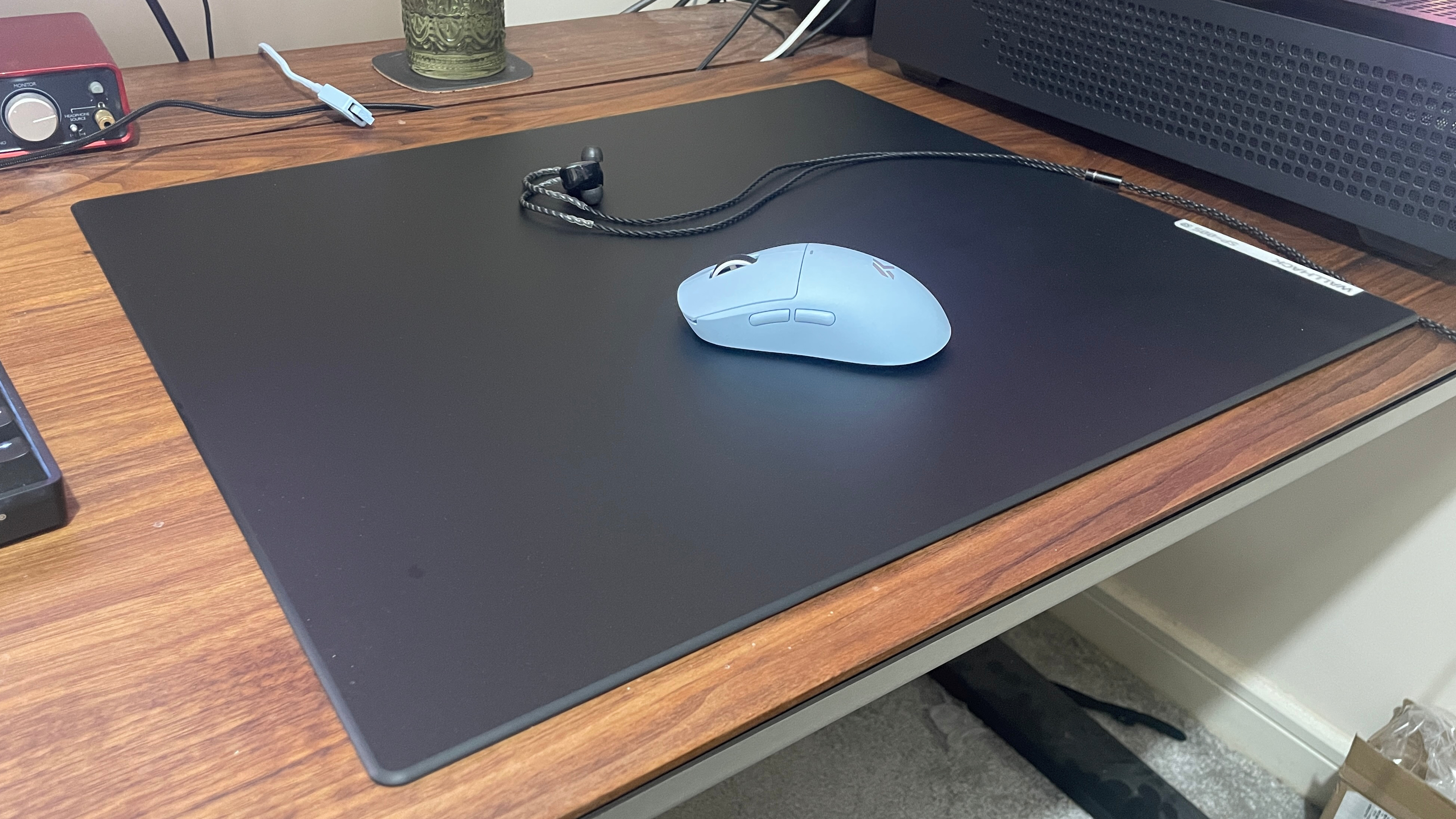 A Wallhack SP-005 glass mouse pad on a desk with a mouse and earphones on top.