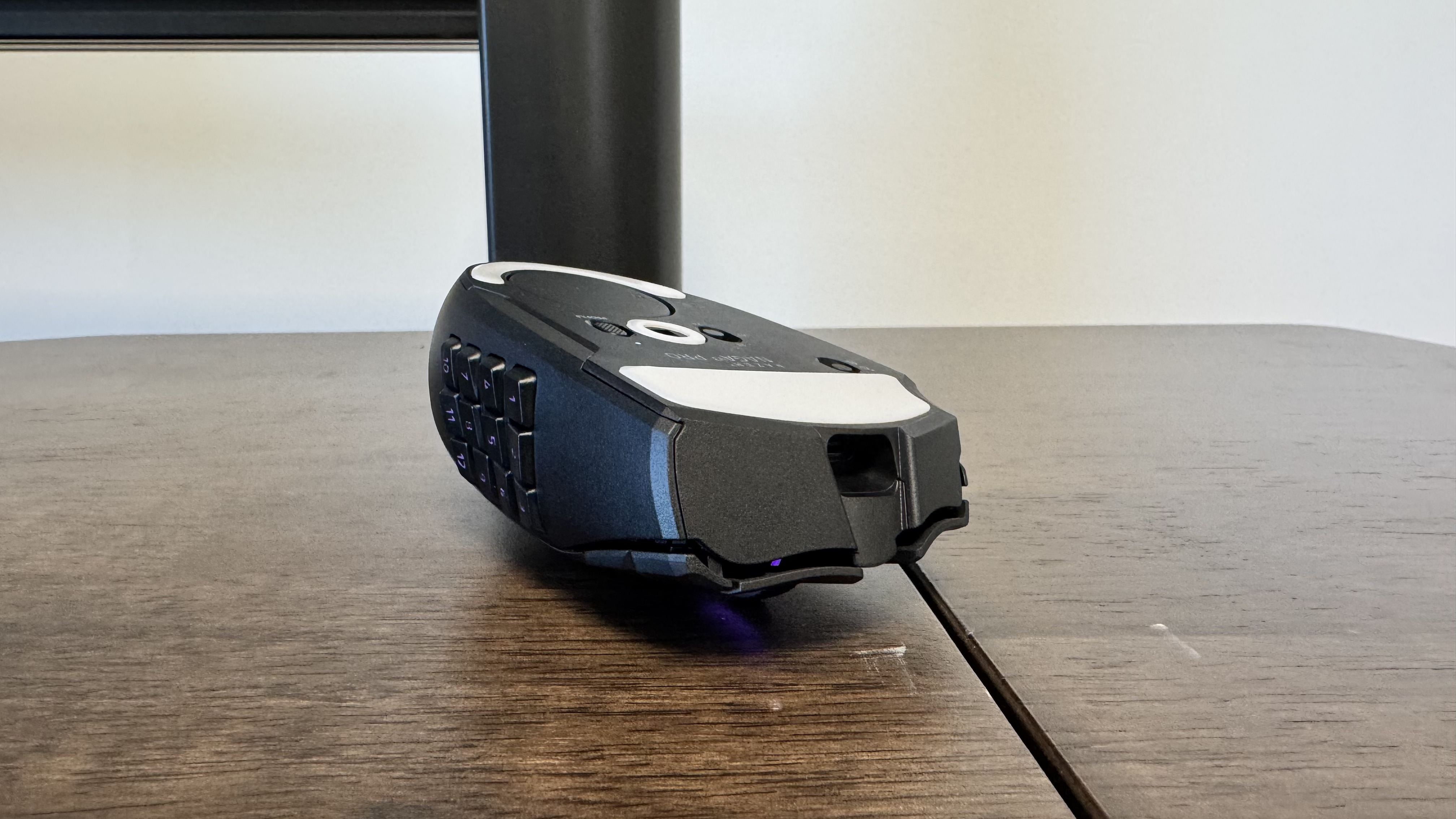 The Razer Naga V3 Pro on a wooden table from the side, with the mouse upside down