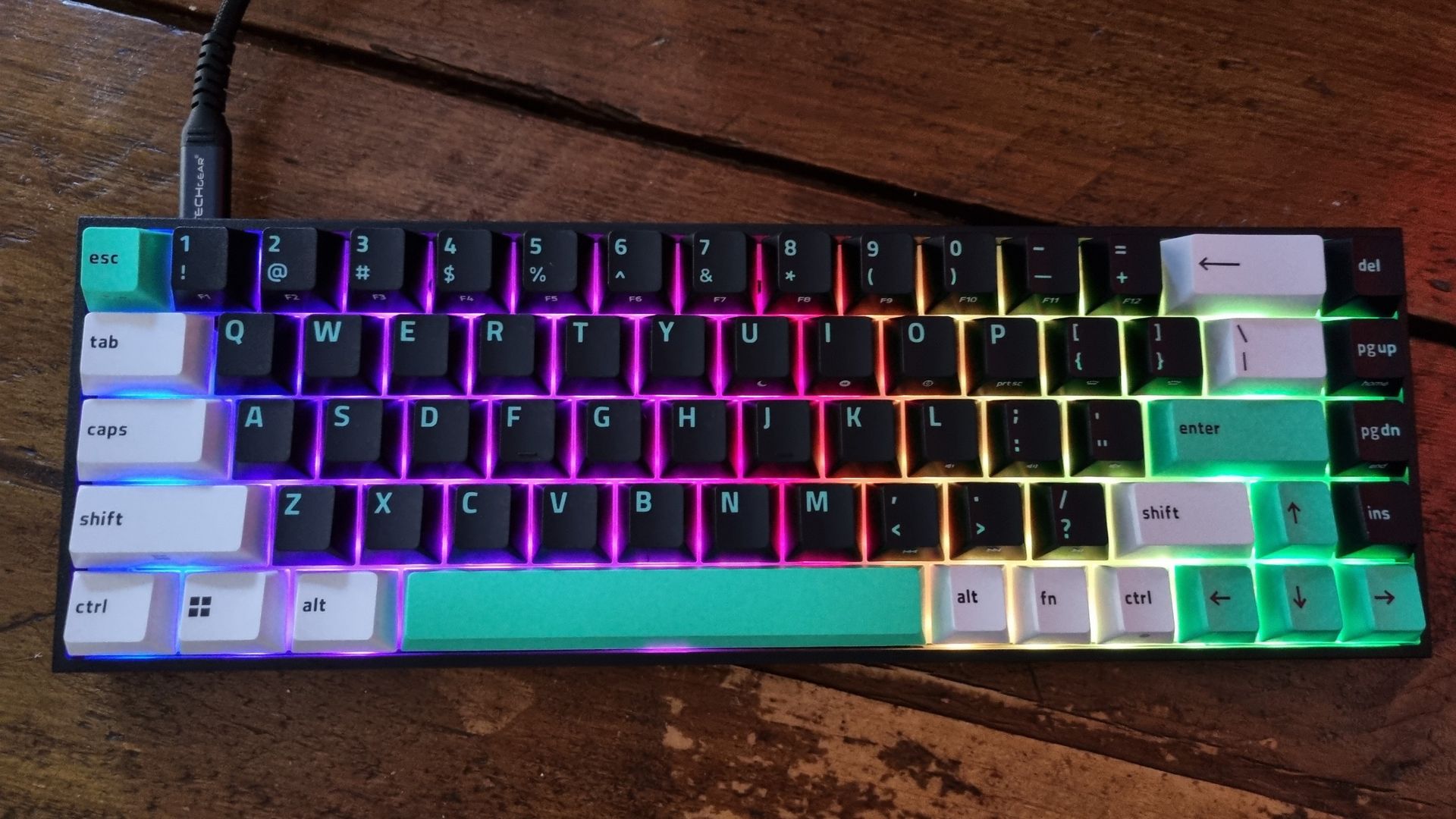A Razer Reclusa X Mini 65% gaming keyboard with rainbow-coloured RGB lighting on a wooden desk